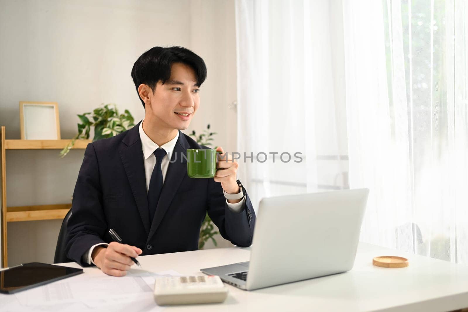 Portrait of smiling young businessman taking a coffee break while working on a laptop.