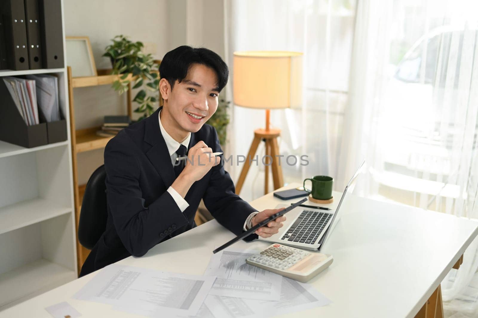 Successful businessman in formal suit using digital tablet at desk.