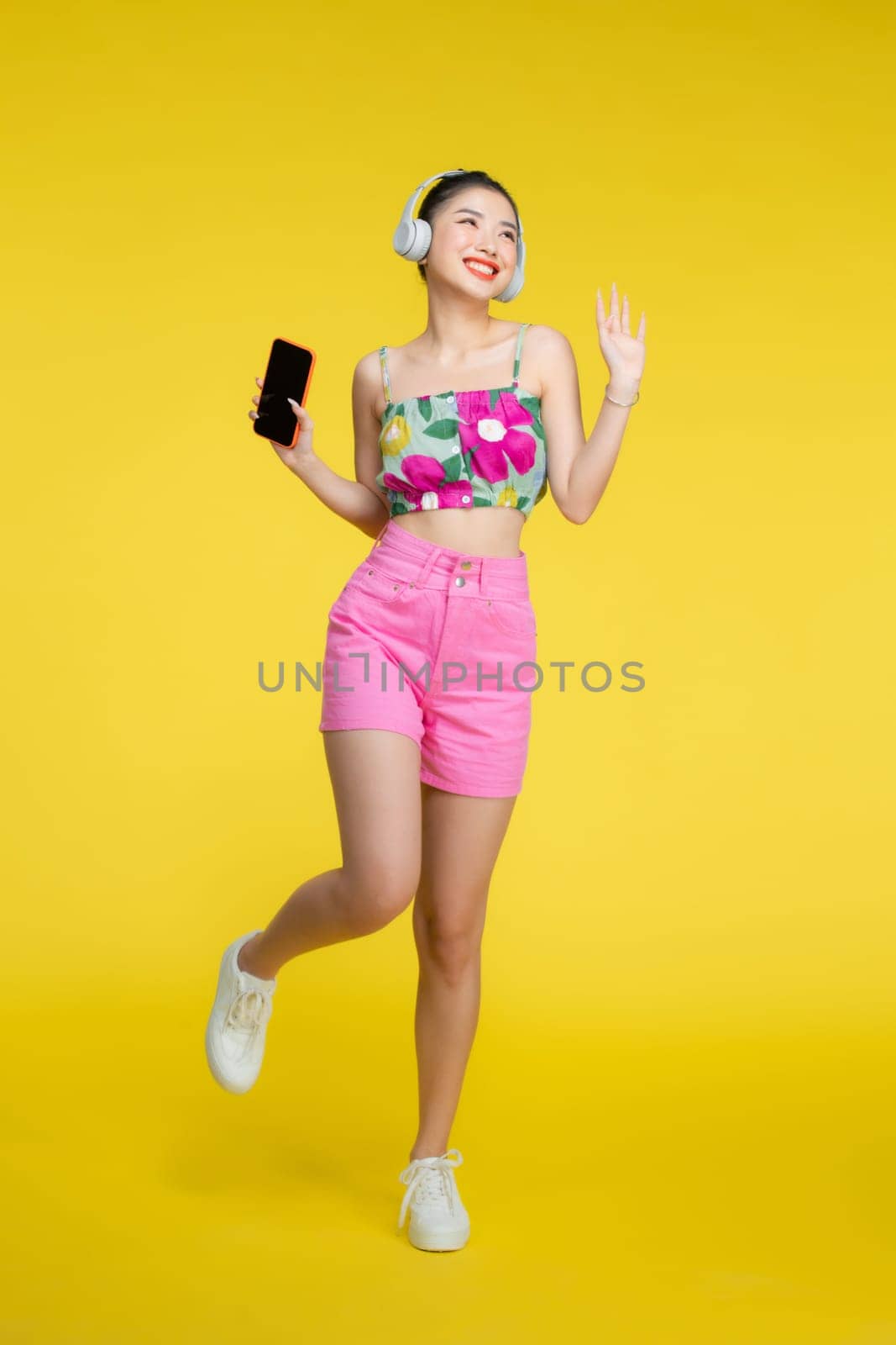 Relaxing beautiful young asian woman is enjoying music and dancing on yellow background