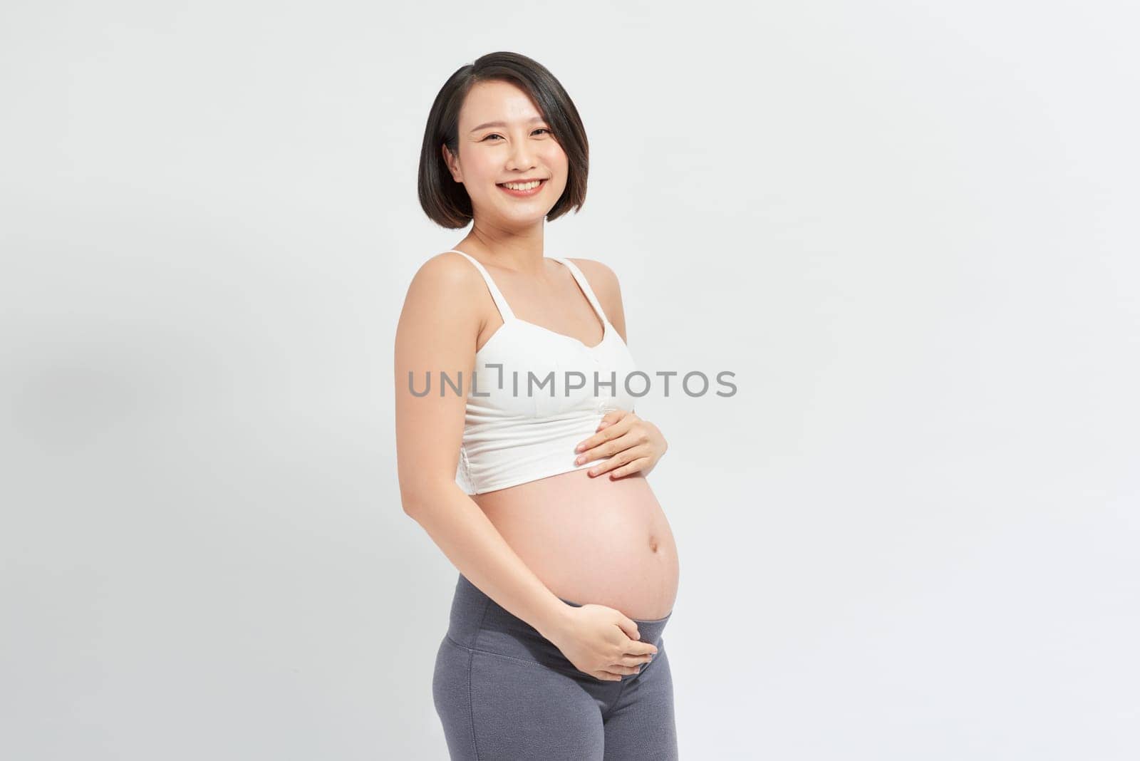 Beautiful asian pregnant woman holding her belly on white background