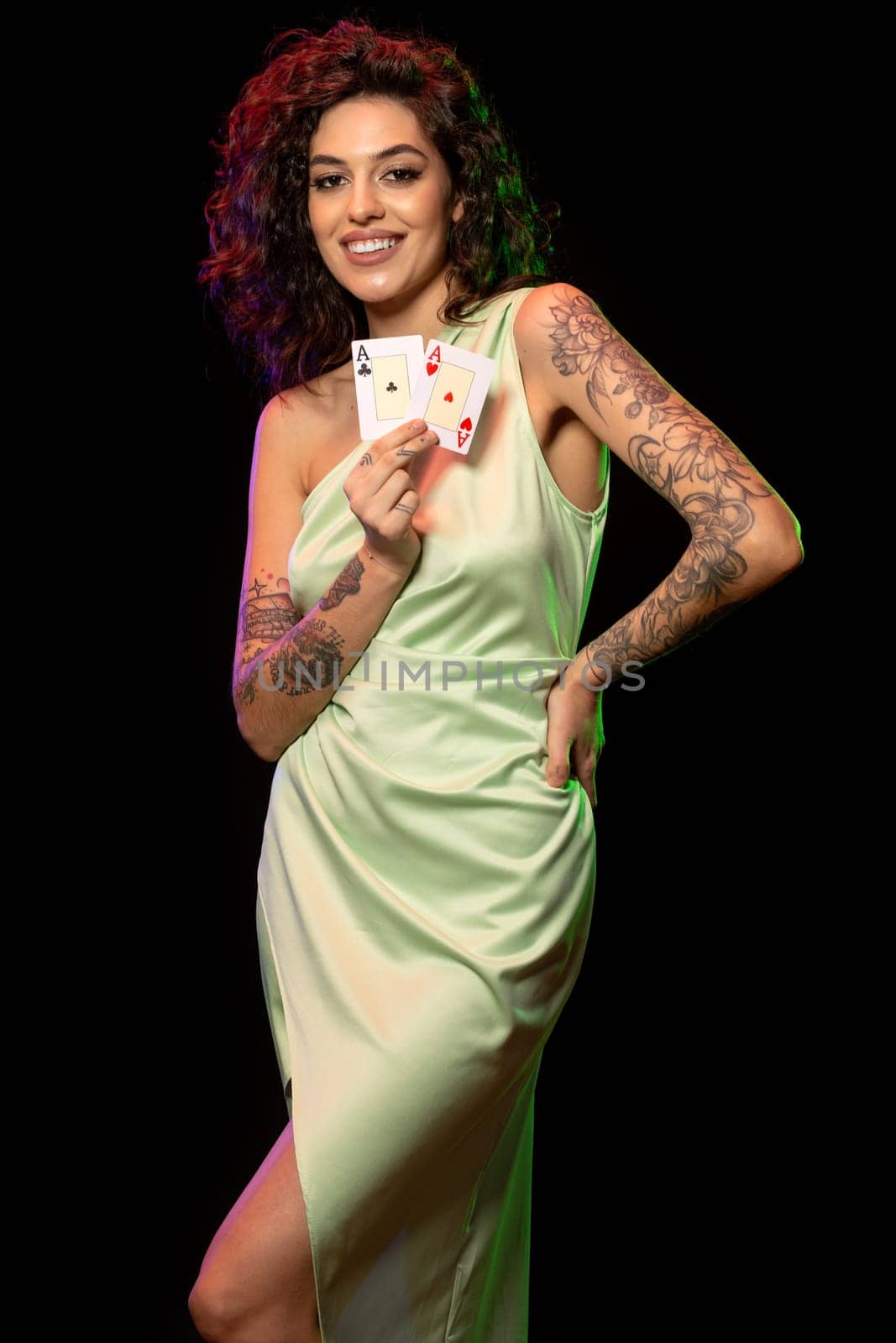 Portrait of laughing stylish young brown-haired woman happy with successful poker game posing against black background, demonstrating set of winning cards from pair of aces