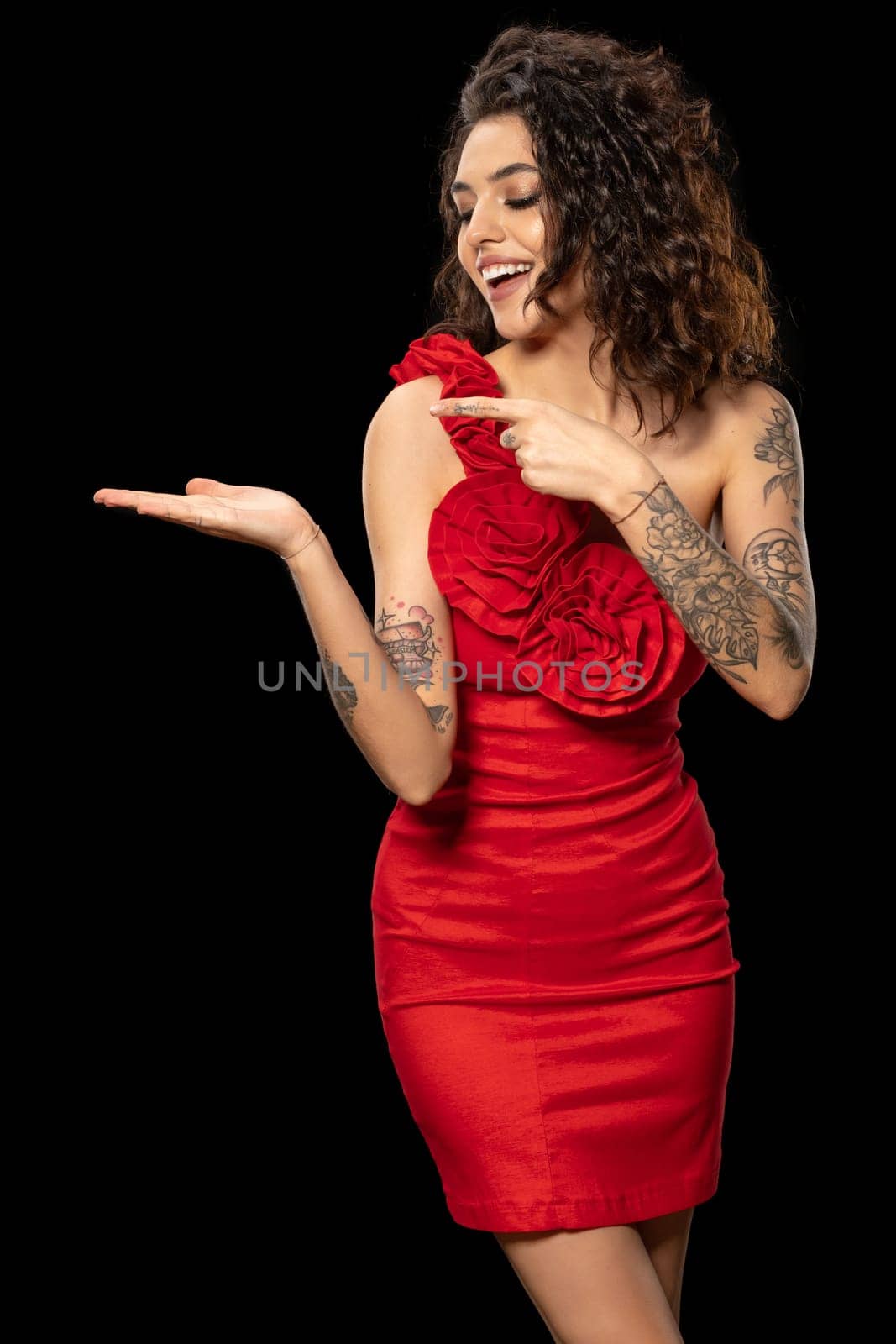 Excited young brunette in red dress pointing at imaginary product on palm by nazarovsergey