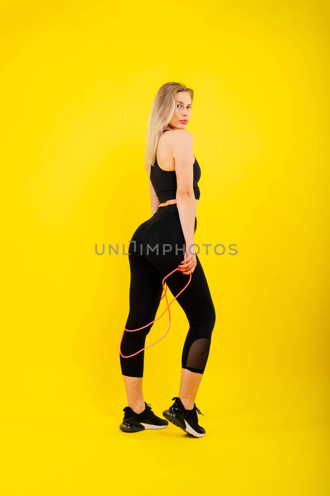 Blond woman with jump rope in studio, yellow red and dark background by Zelenin