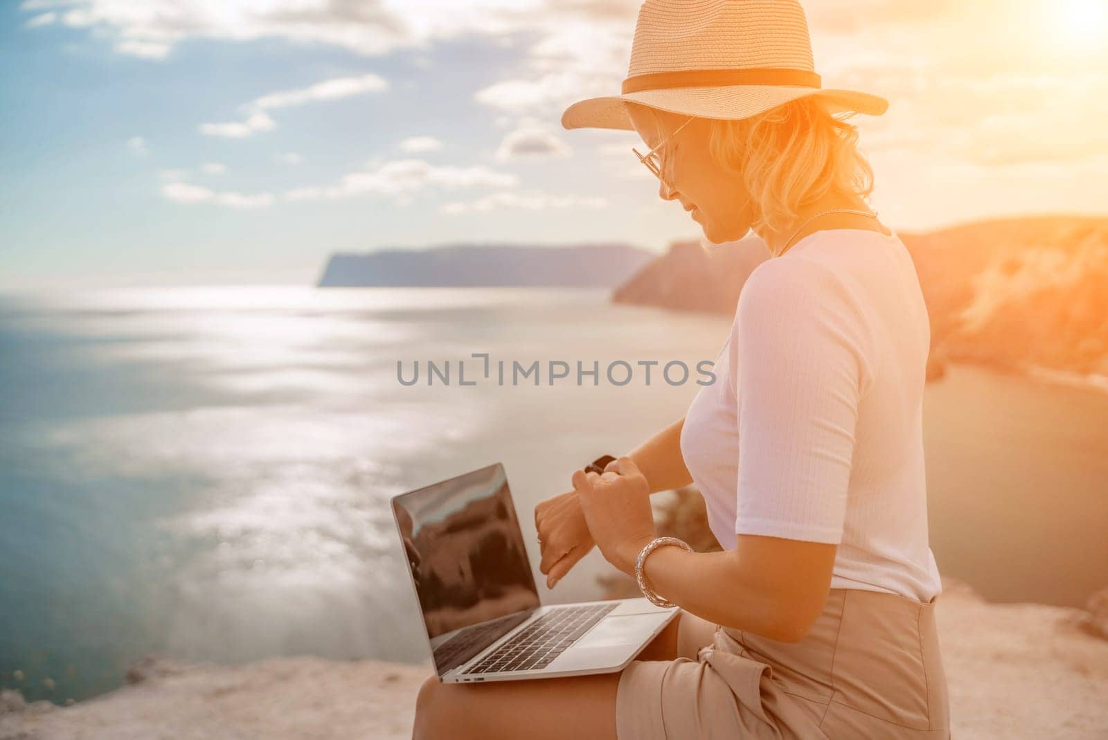 Freelance women sea working on the computer. Good looking middle aged woman typing on a laptop keyboard outdoors with a beautiful sea view. The concept of remote work