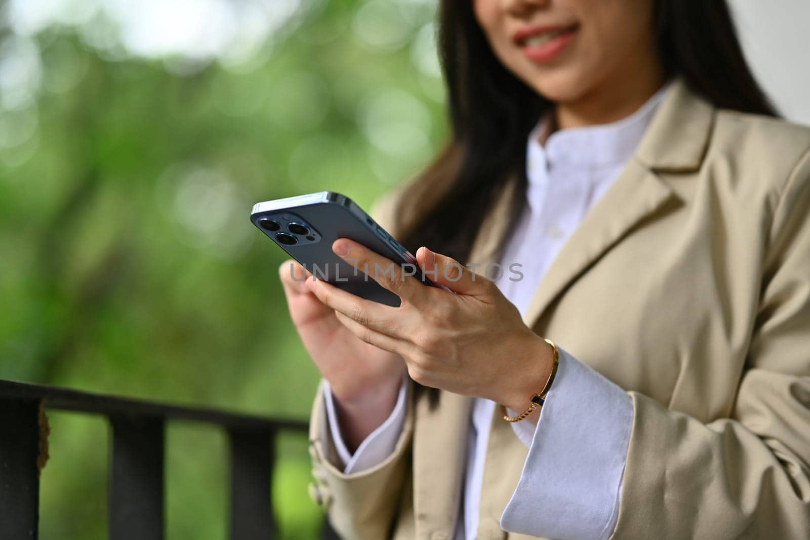 Pleasant businesswoman texting messages, chatting in social on smartphone while sitting outside office building.