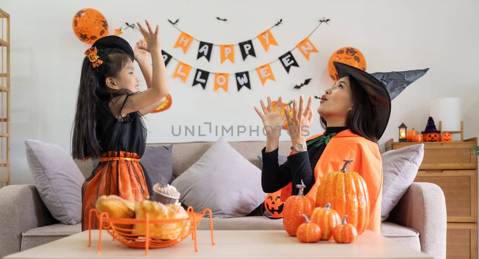 Happy family mother and child happy girl with Halloween at home together beautifully decorated. pretending to release air from a balloon at a child girl by nateemee