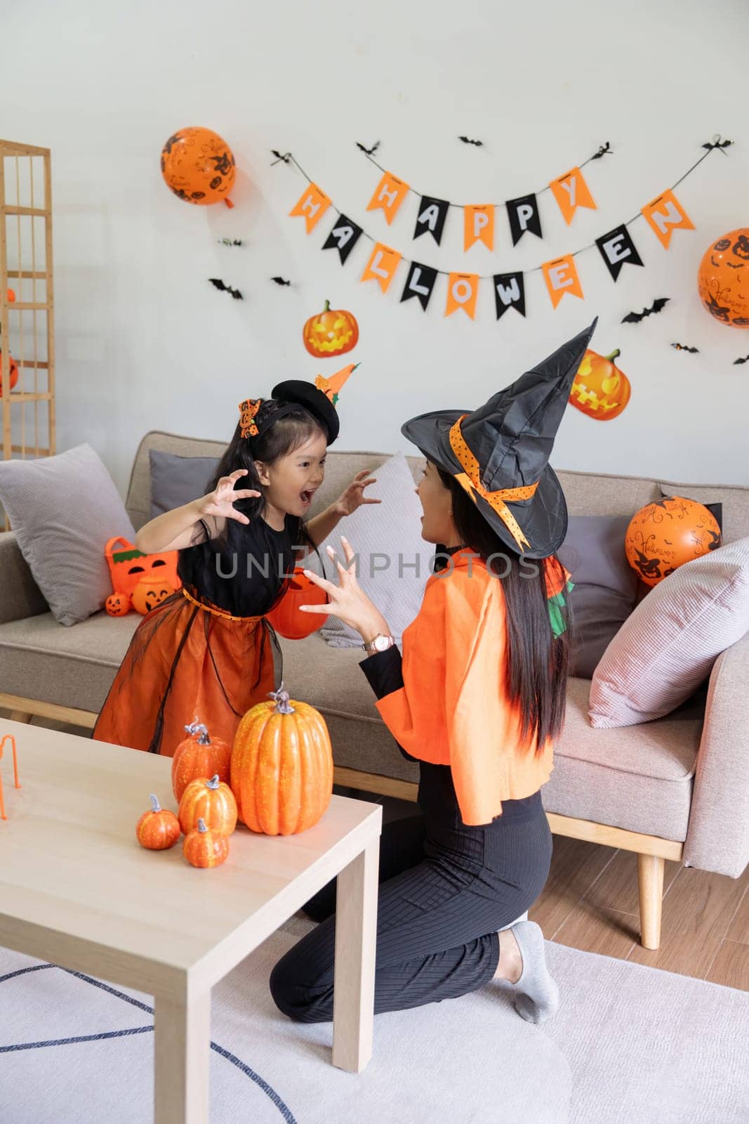 Happy family mother and child happy girl with Halloween at home together beautifully decorated. Mother teasingly playing with daughter by nateemee