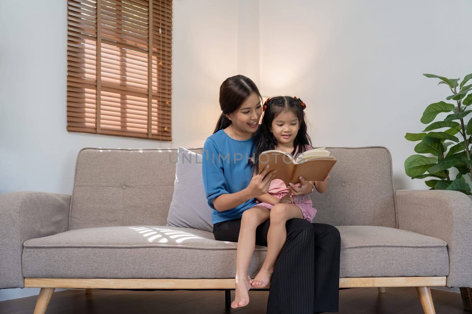 Mother and daughter read together on the sofa at home by nateemee