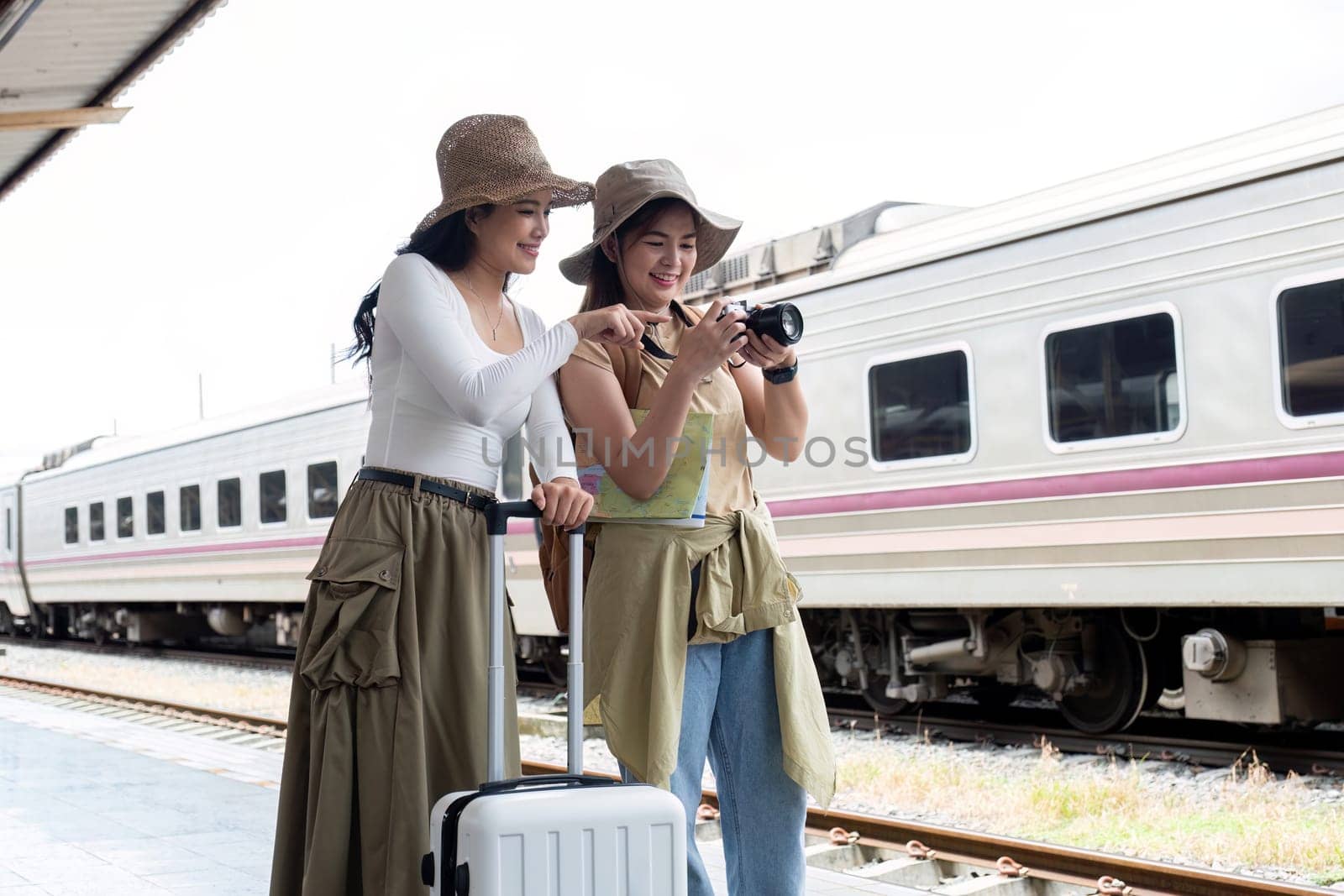 Two beautiful female tourists pose for a photo at the train station. While waiting to board the train for a holiday together.