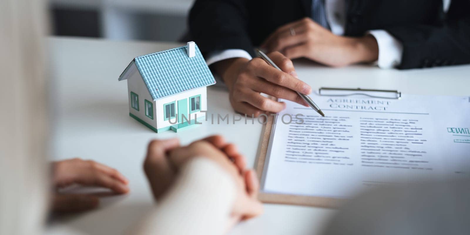 Young Asian couple making contract with house sale agency. man and his wife sitting signing the contract next to him looking the contract document with smile. real estate agreement successful concept.