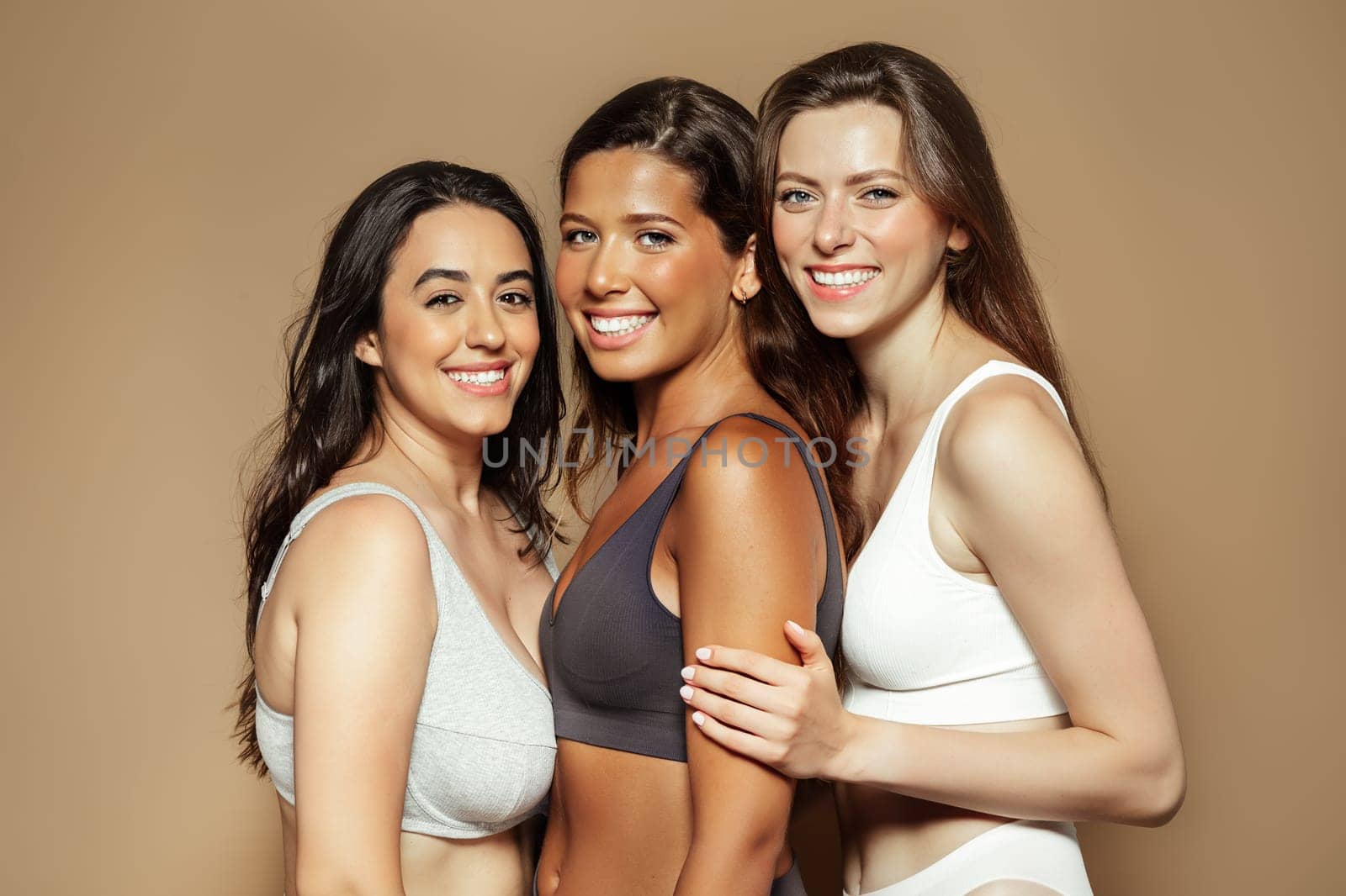 Positive millennial diverse women in underwear enjoy beauty care, isolated on beige background, studio. Dermatology and motivation for self love, spa treatments, wellness and healthy skin care