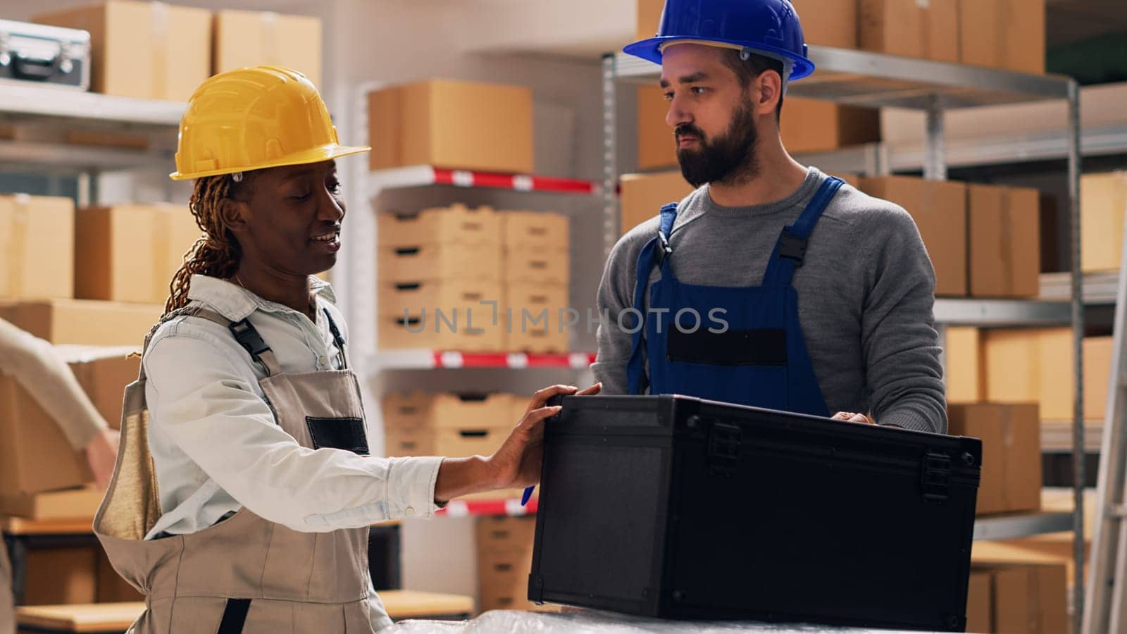 Multiethnic team of people examining list of products on files, talking about merchandise stock for inventory. Man and woman in overalls checking goods in storage room depot, industrial work.