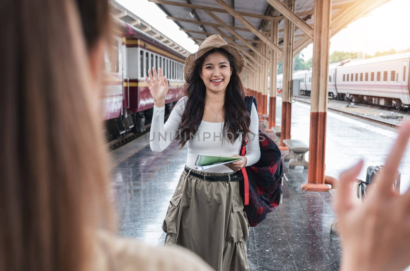 young female tourist smiles and greets a fellow passenger she just met while waiting for a train at the train station. by wichayada