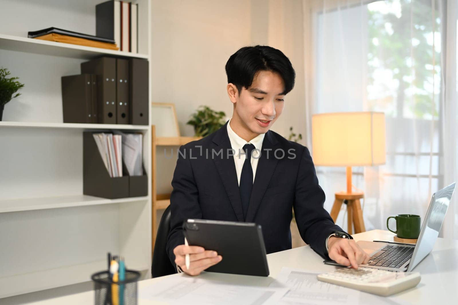 Successful businessman in formal suit using digital tablet at desk.