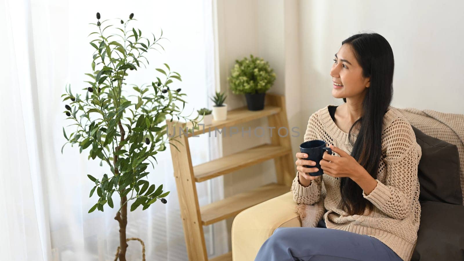 Peaceful young woman enjoying a hot drink and gazing out the window.
