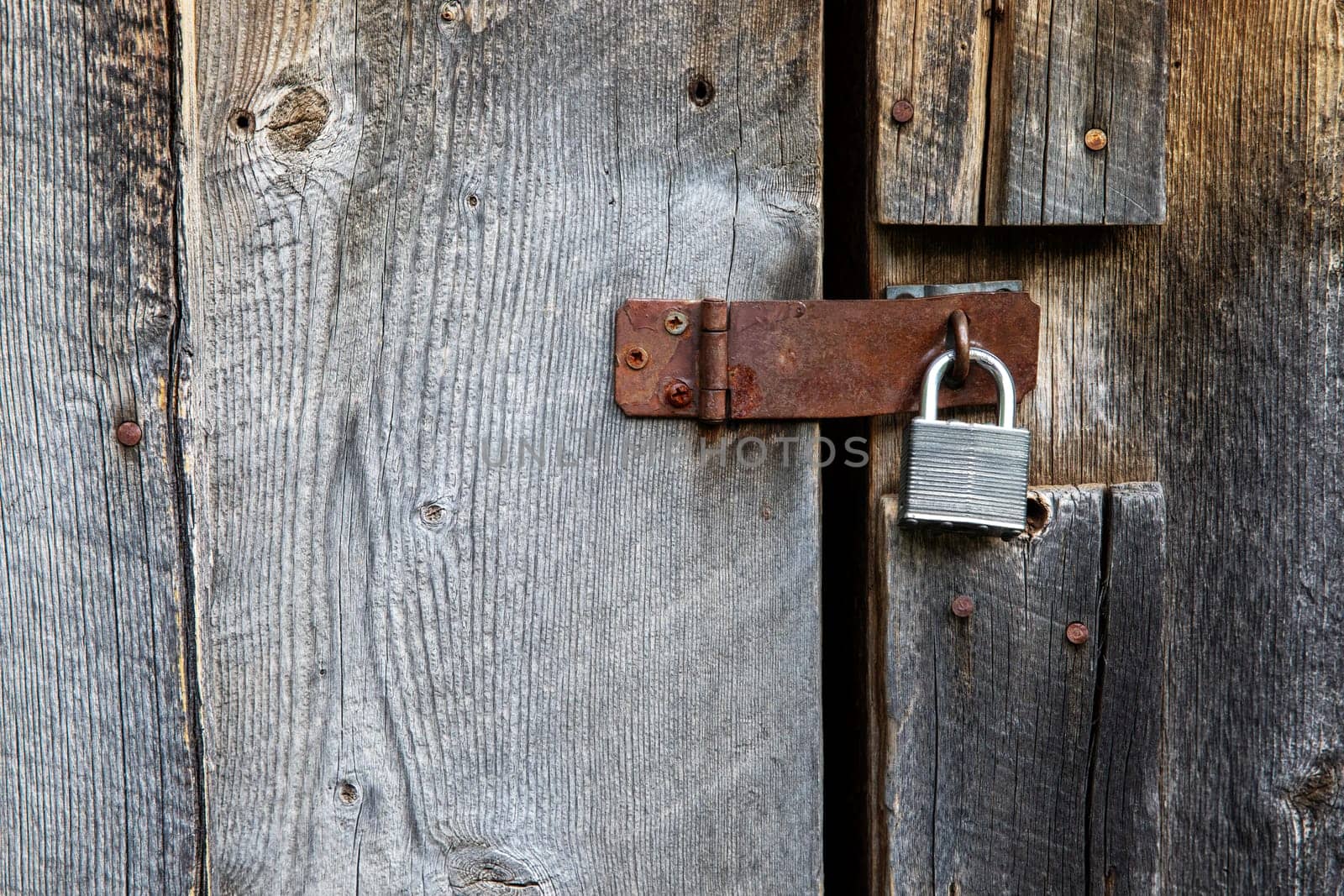 Close-up of a rustic wooden door featuring a rusty padlock, emphasizing security and rustic vintage design elements. The texture highlights aged wood and metal.