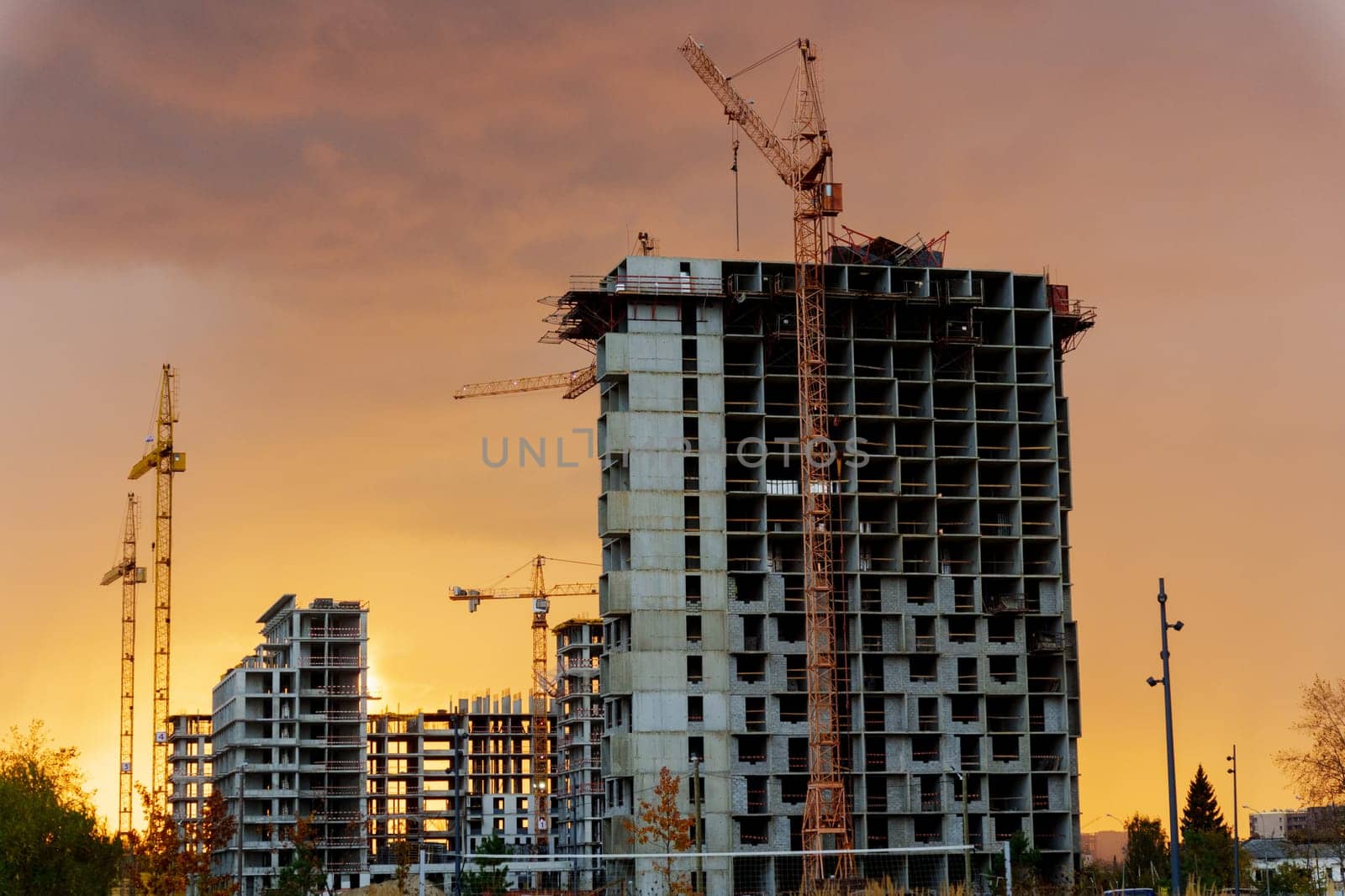 Golden sunset behind a bustling construction site with cranes and buildings silhouetted against the vibrant sky