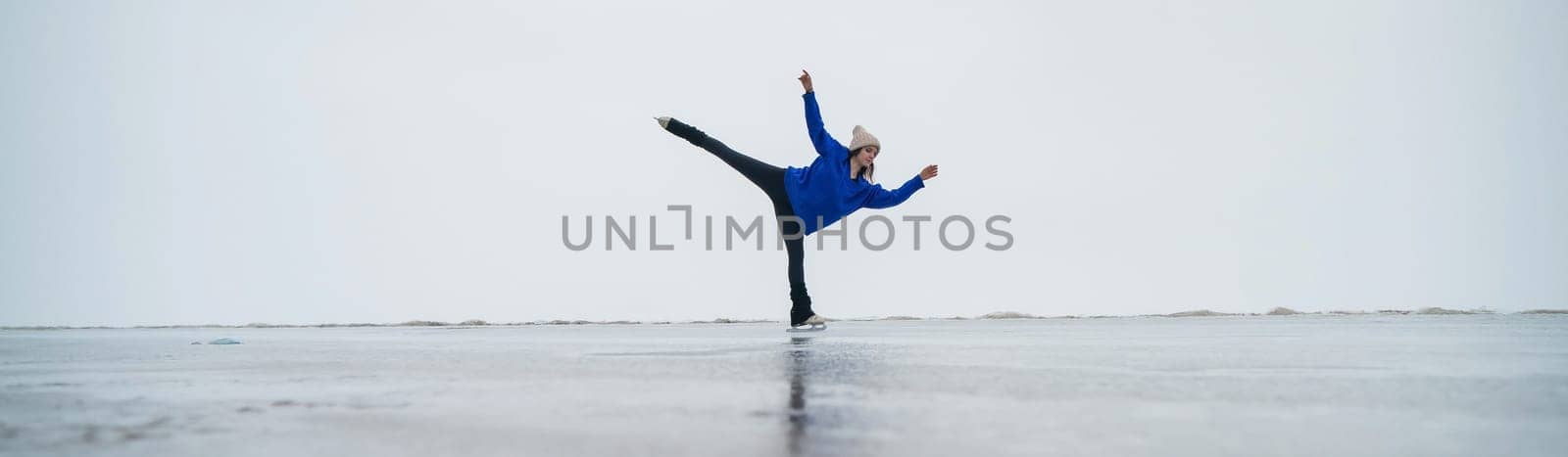 Caucasian woman in a blue sweater is skating on a frozen lake. Figure skater performs a swallow