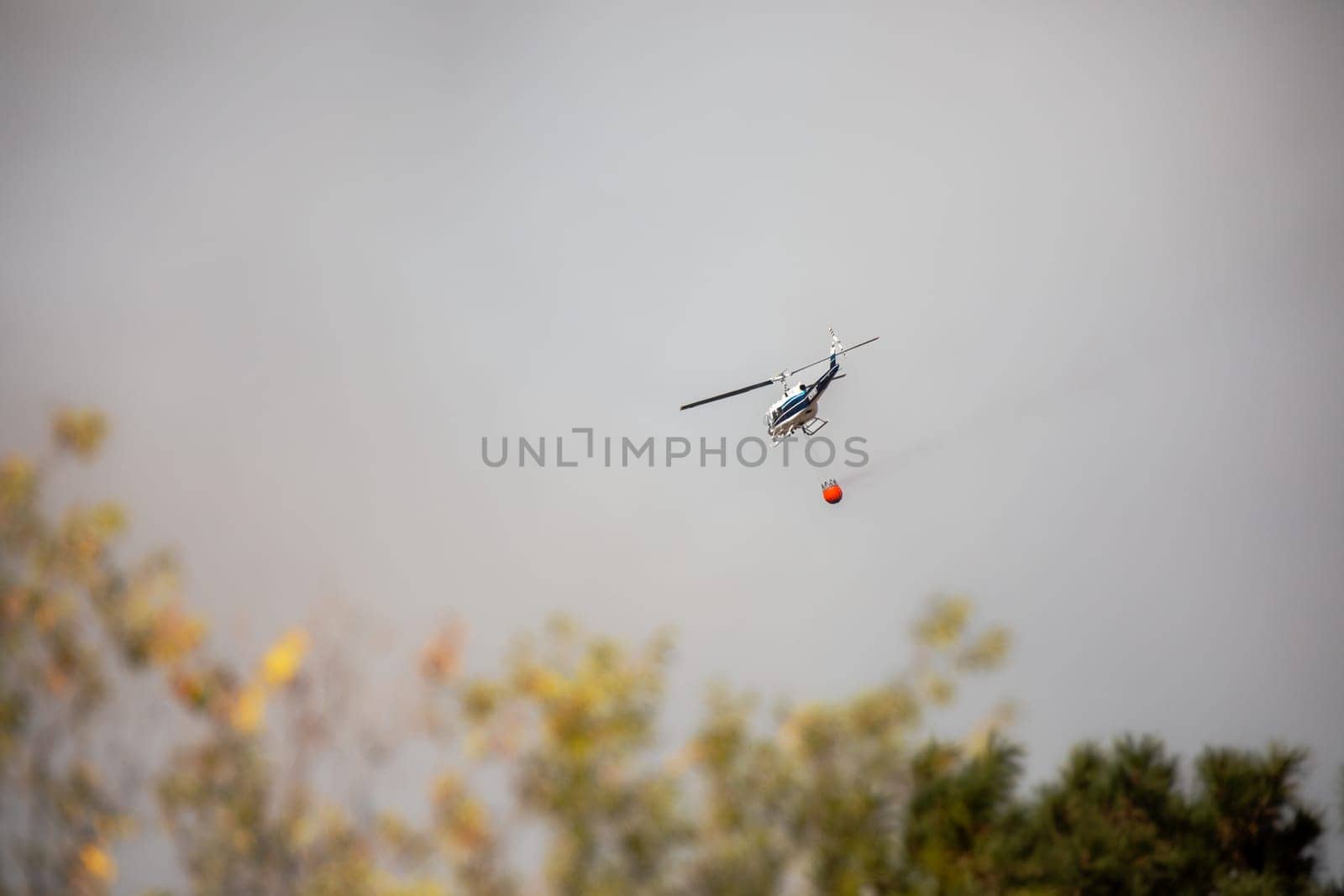 Helicopter performs aerial firefighting, carrying a large water bucket over smoky landscape to combat a widespread blaze of the 2024 Valley Fire near Boise, Idaho