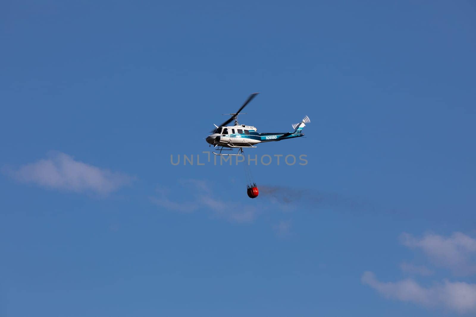 A helicopter carries a water bucket in flight, demonstrating aerial firefighting techniques. Captured against a clear blue sky while fighting the 2024 Valley Fire near Boise Idaho