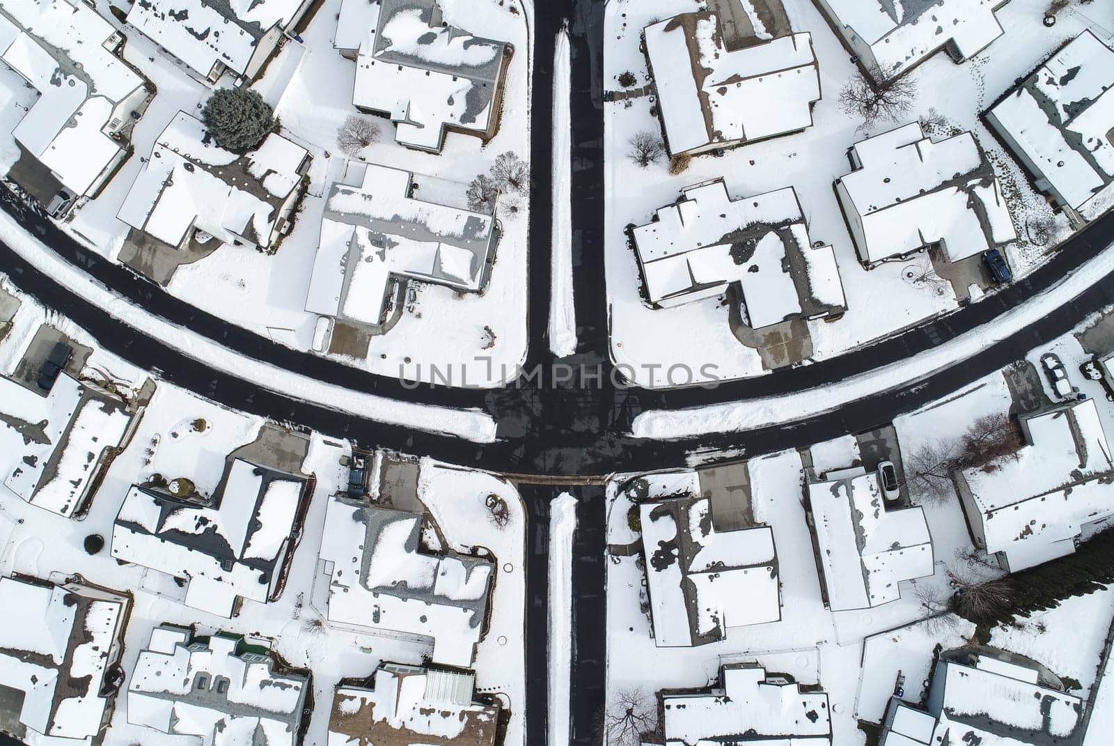 Aerial shot featuring a snow-covered suburban neighborhood during winter. The intersecting streets and snow-laden rooftops create a serene and symmetrical winter landscape.