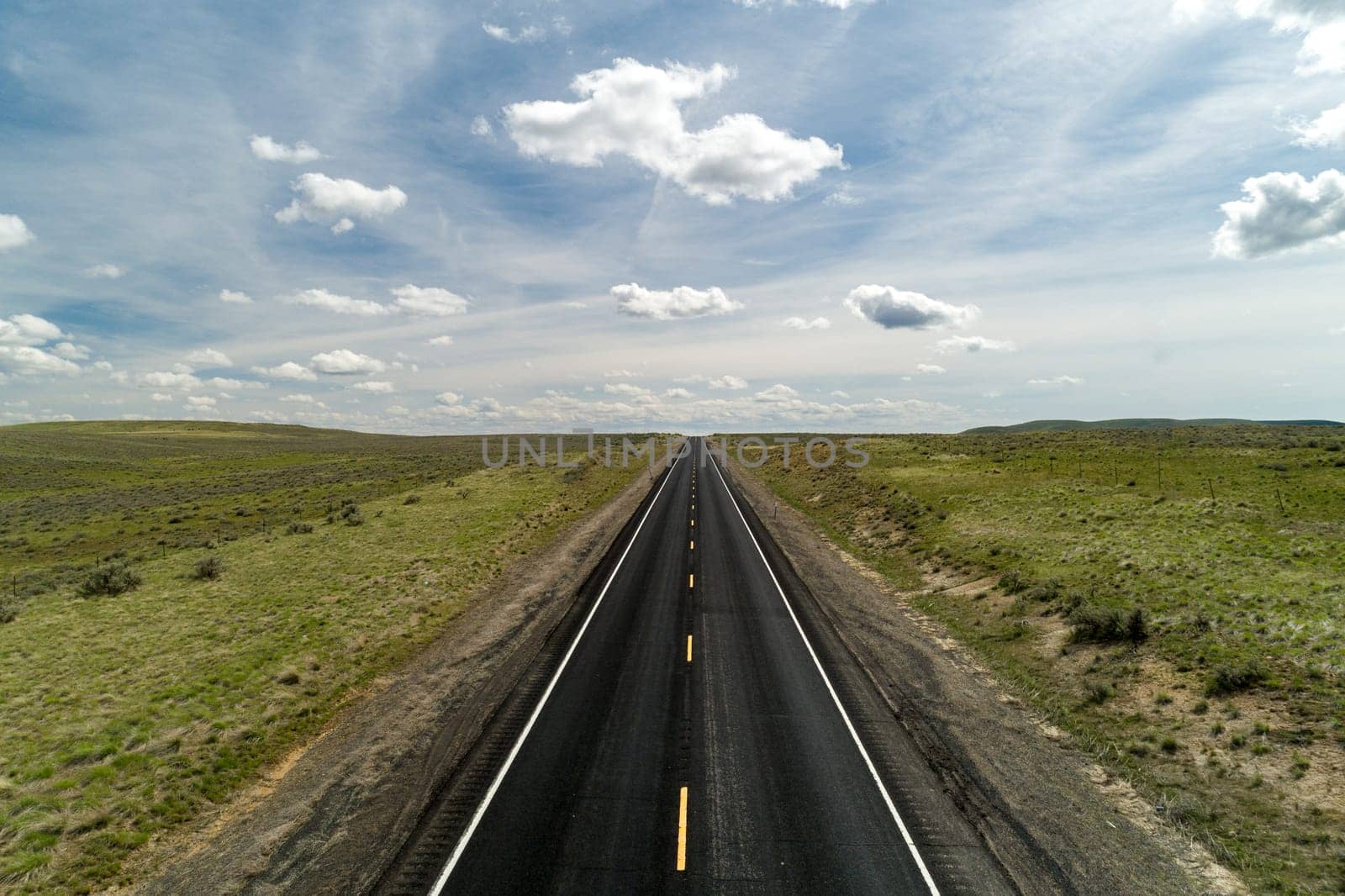 A vast open road stretches towards the horizon, surrounded by green fields under a sky with scattered clouds. Perfect for concepts of freedom and exploration.