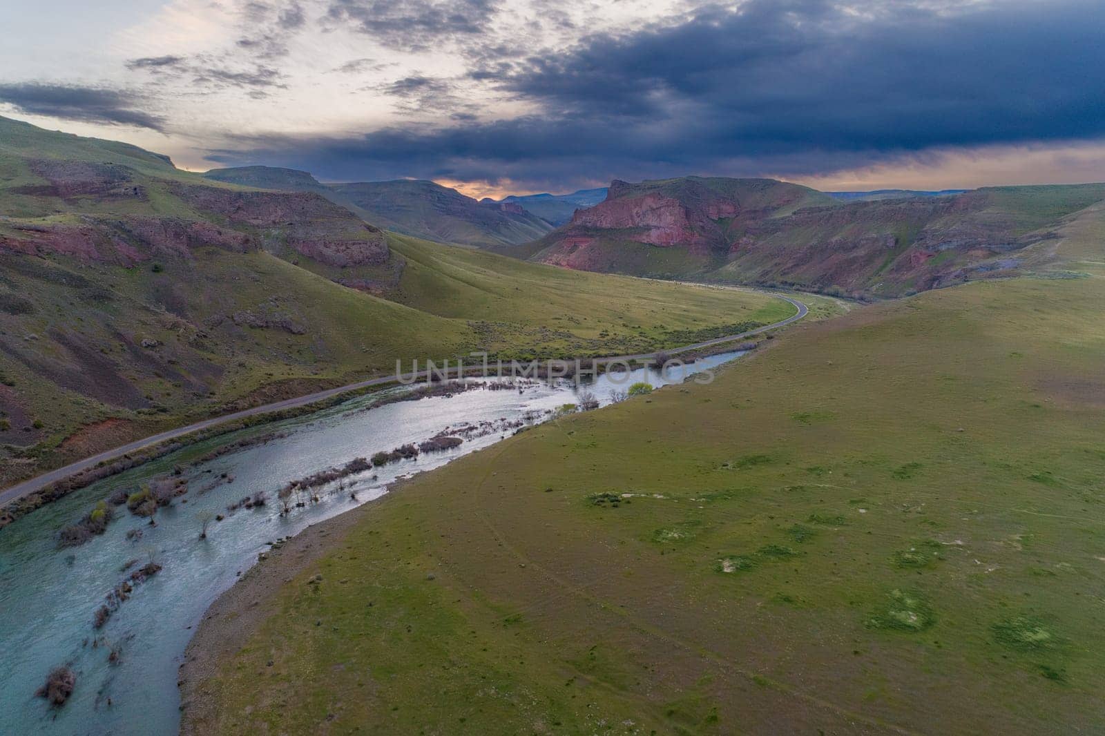 A breathtaking aerial view of a tranquil river winding through a wide, expansive valley surrounded by rolling hills and dramatic skies in Idaho
