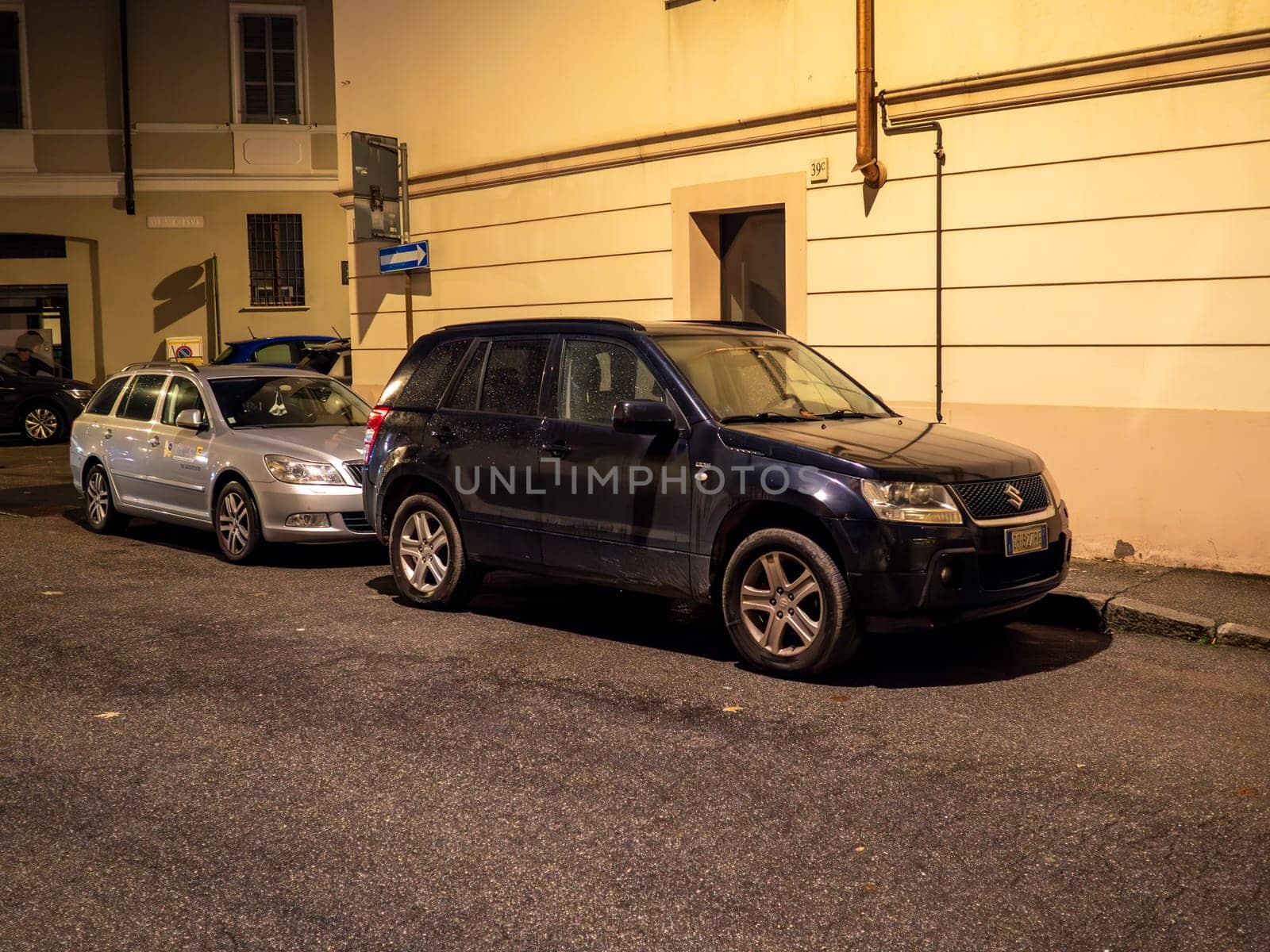 Cremona, Lombardy, Italy October 15th 2024 Two cars parked on a narrow street at night, illuminating the building facades and creating a peaceful urban scene