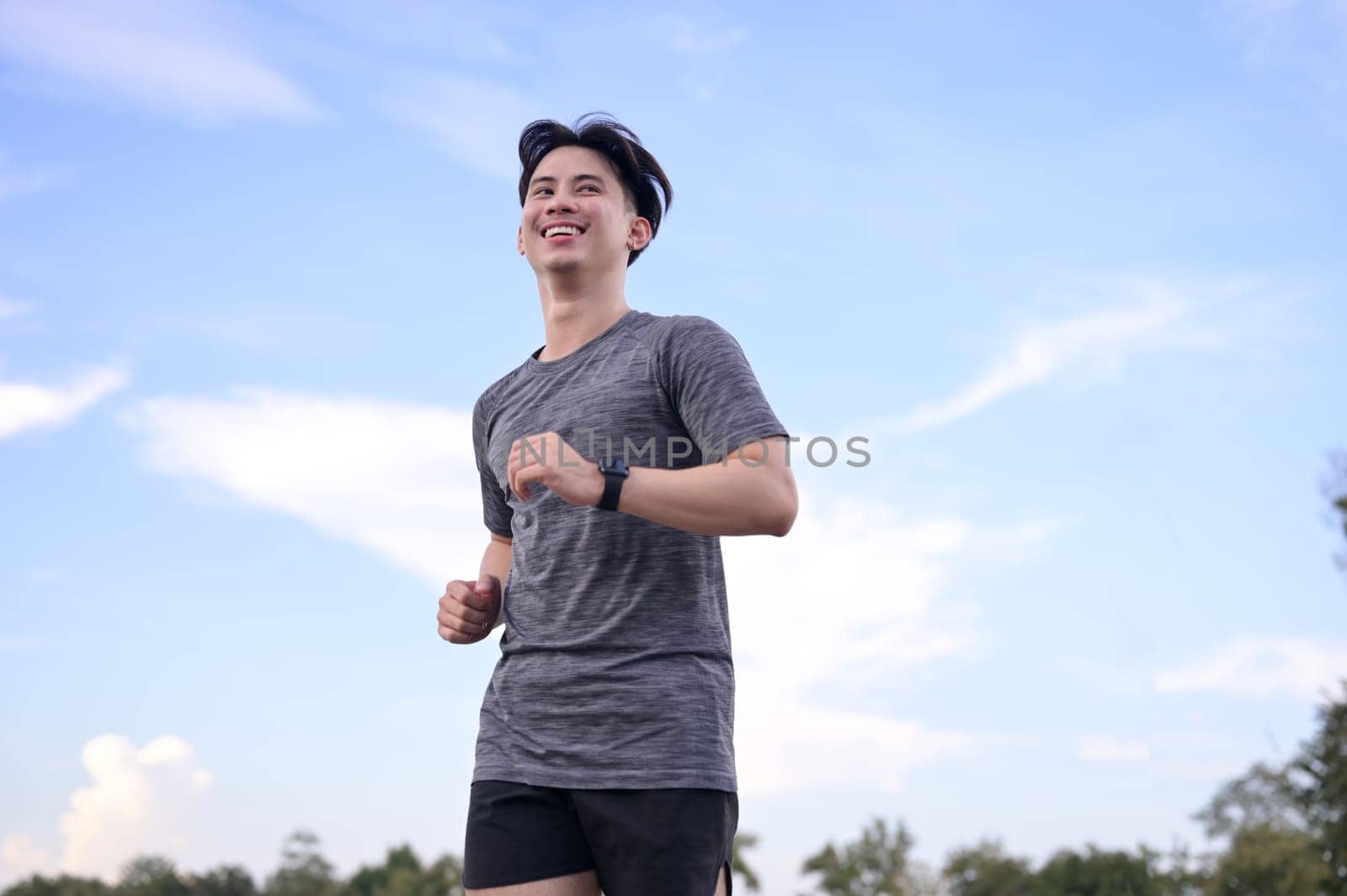 Happy smiling man jogging through a park during the late afternoon.