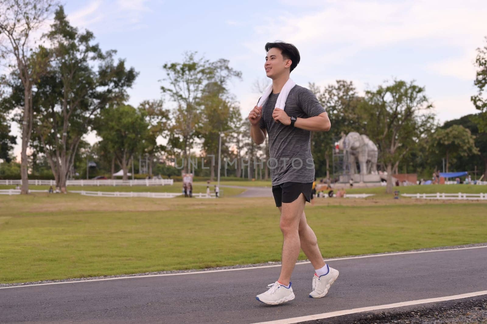 Happy smiling man jogging through a park during the late afternoon.