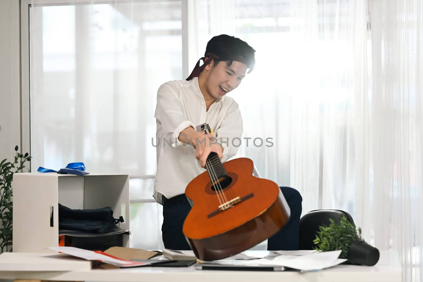 Furious angry male employee smashing guitar on his office desk.