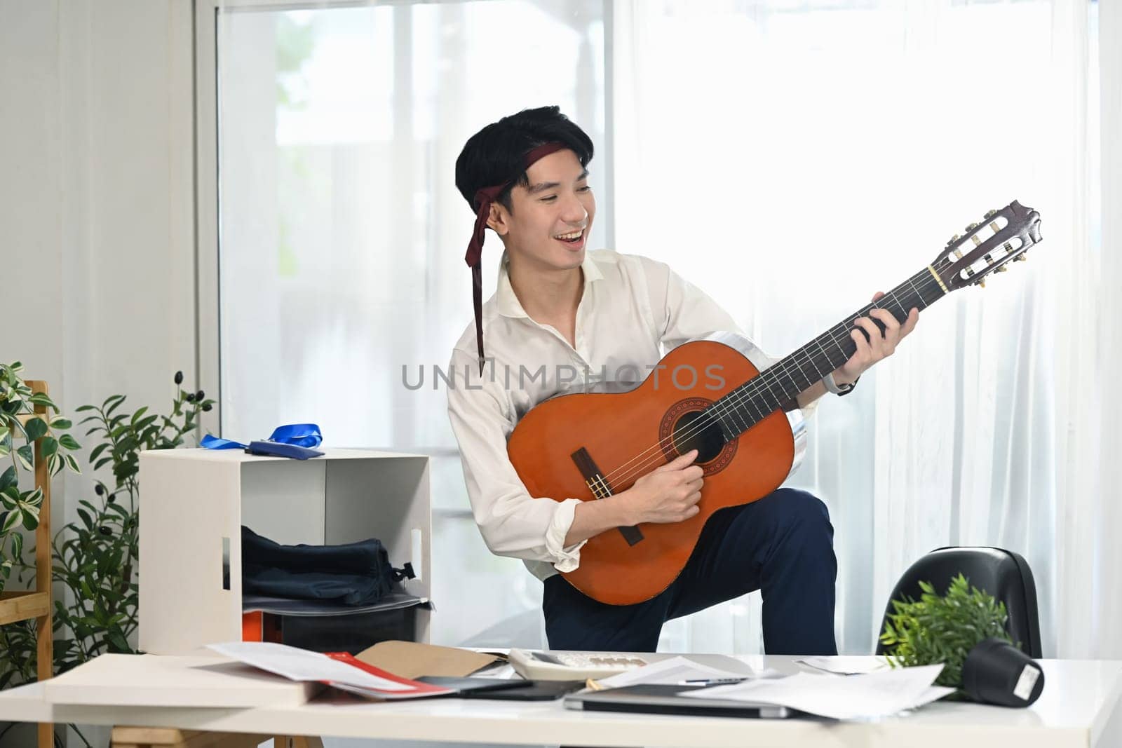Energetic employee in white shirt with necktie around his head enjoying a music break amidst busy workday.