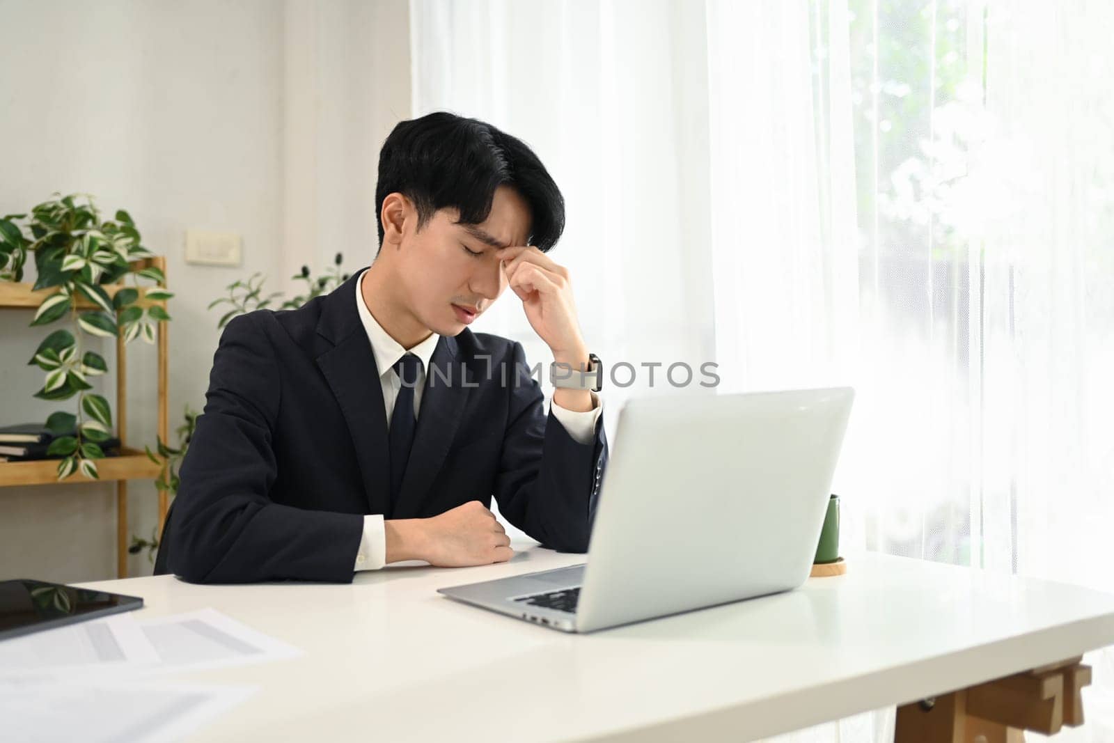 Frustrated young businessman in a business suit holding his head in hands sitting at desk.