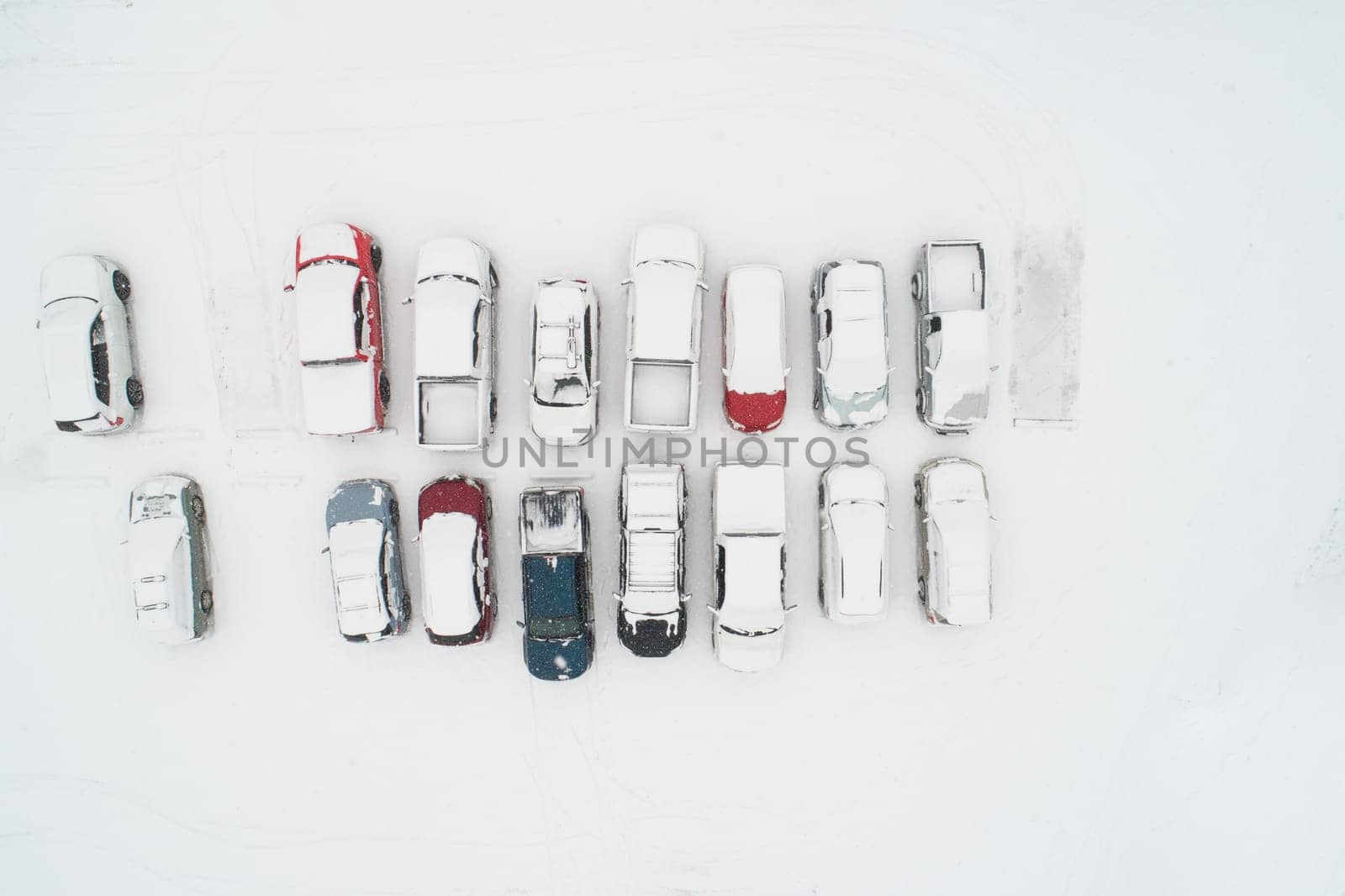 Aerial shot of parked cars covered in a thick layer of snow, showcasing winter's serene and chilly beauty. Captures the contrast of vehicles against the snowy landscape.