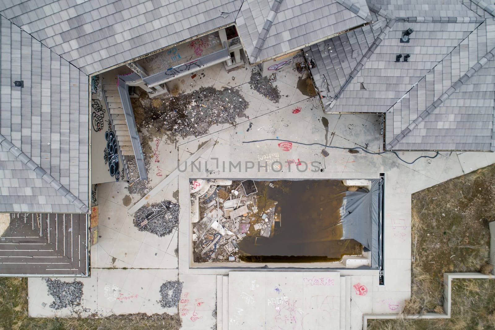 Top-down view of a neglected building featuring graffiti and scattered debris. The dilapidated structure and empty premises evoke themes of urban decay and abandonment.