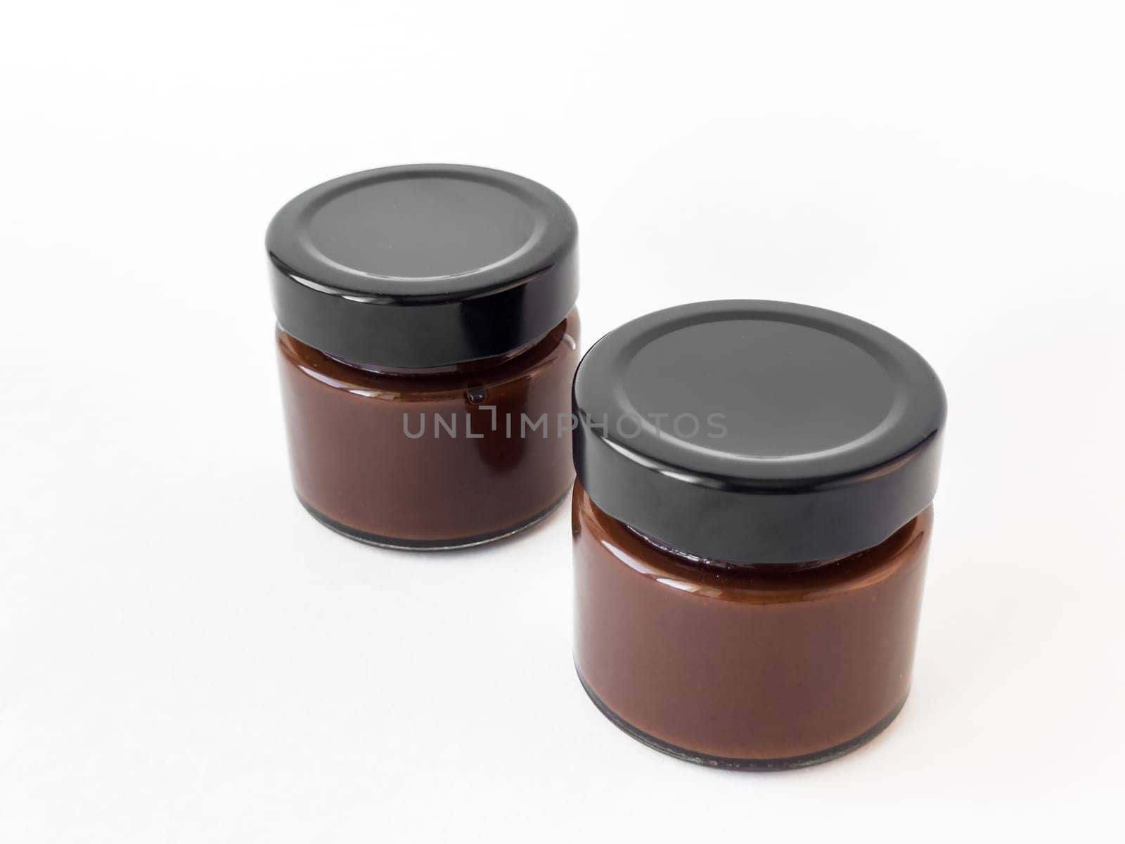 Two glass jars of chocolate spread on white background.