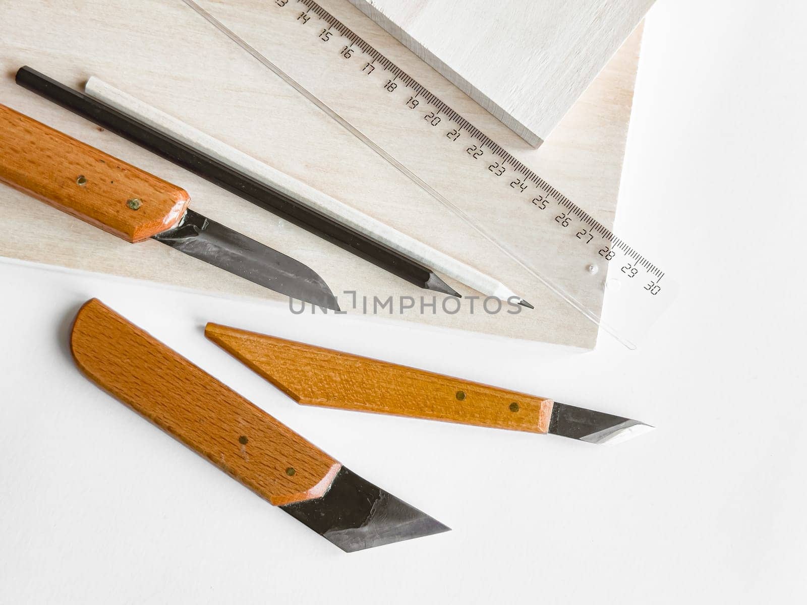 Crafting essentials. Precision knives, ruler, and pencil on wooden surface.