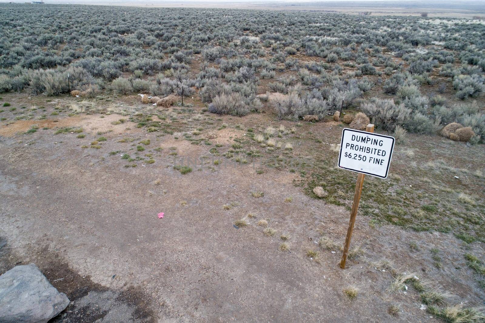 A wide view of a desert landscape featuring a sign warning of a fine for dumping. The terrain is sparse, emphasizing rules and environmental care.