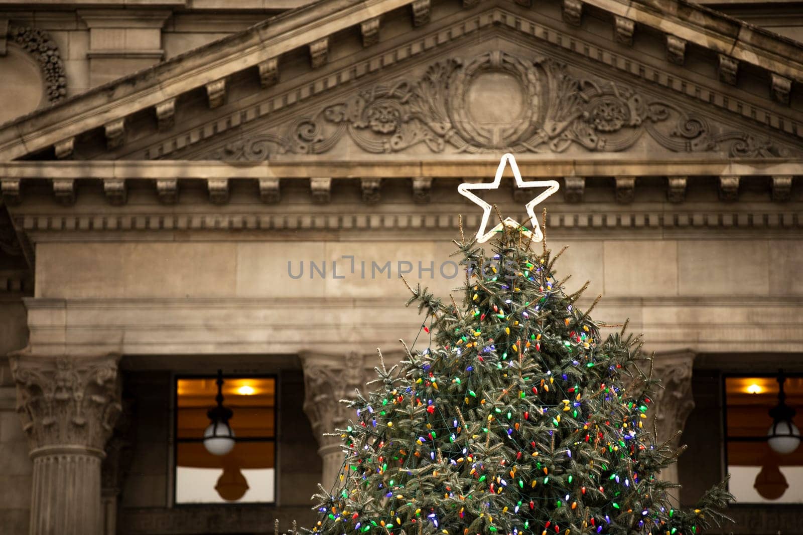 five pointed star on the top of a decorated christmas tree with a fancy building in the background