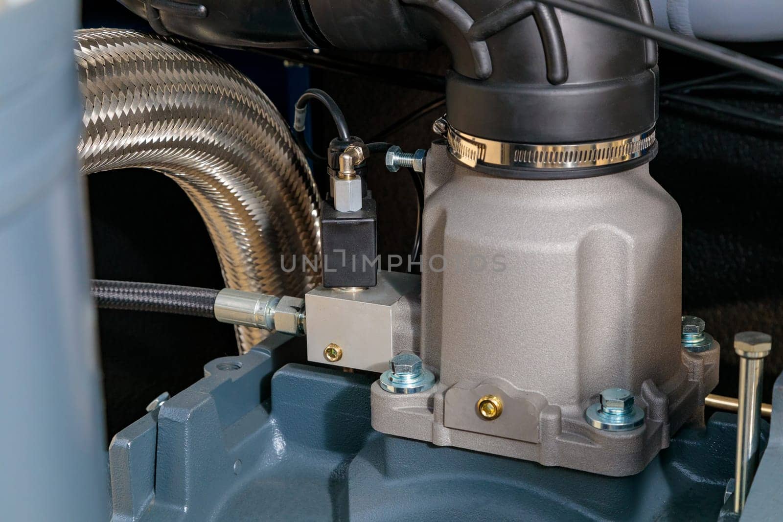 Close-up of an industrial air compressor pump featuring a flexible metal hose, valves, and various mechanical components