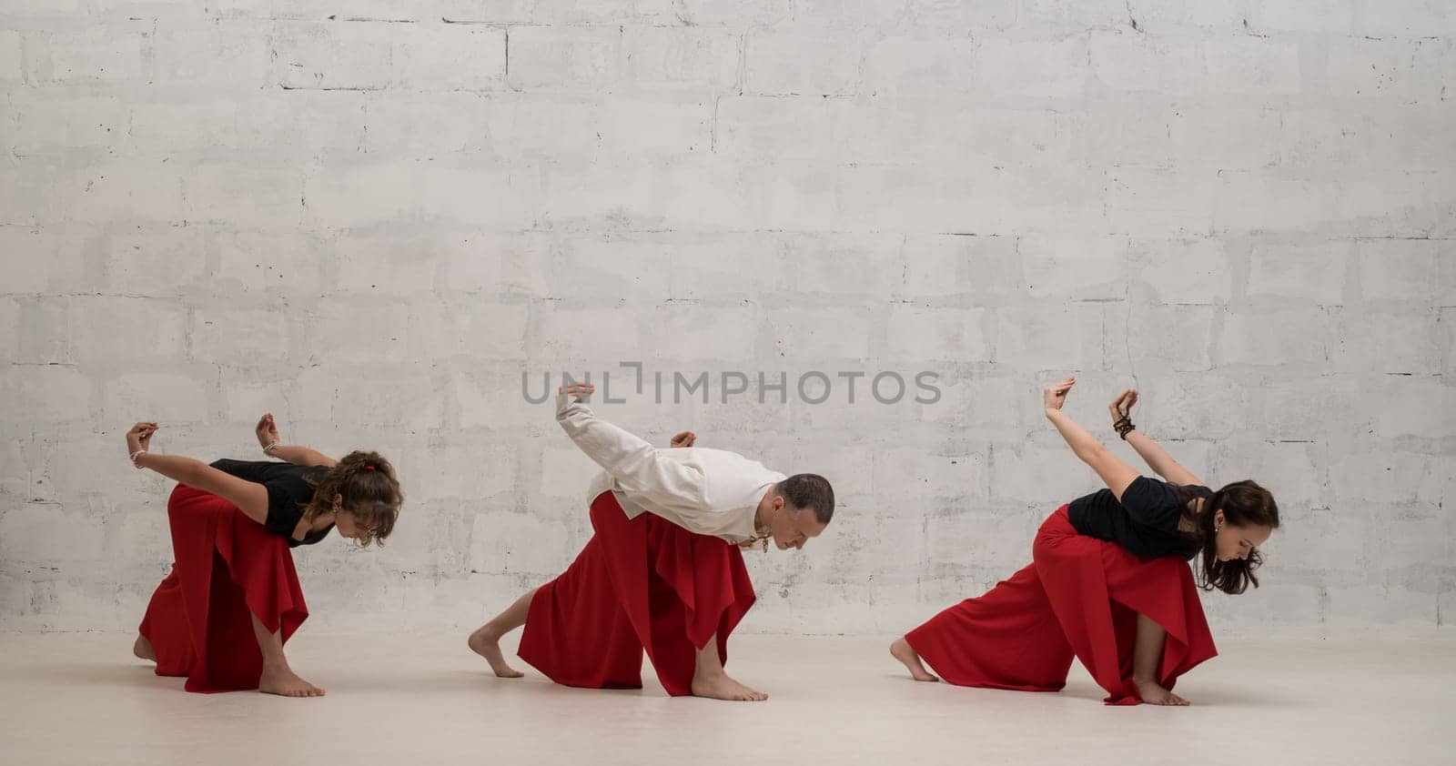 Two women and their male trainer doing yoga exercises view against brick wall