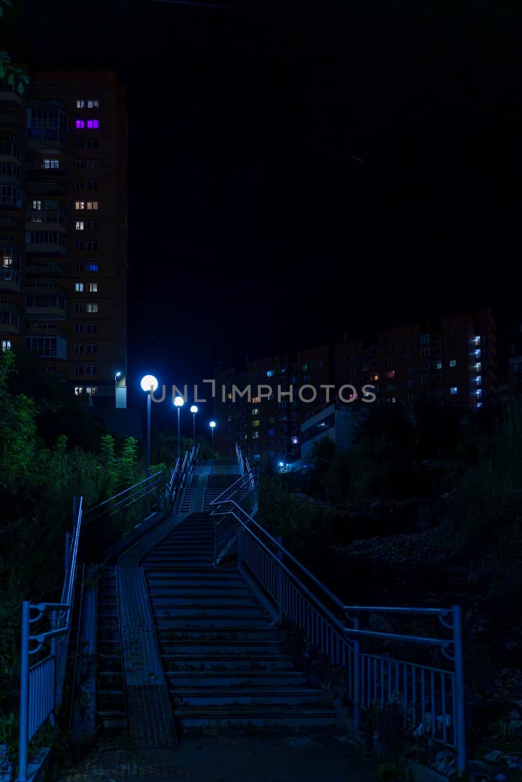 An urban stairway illuminated by streetlights leads up between apartment buildings at night. The quiet and empty scene captures a peaceful residential area with no people visible