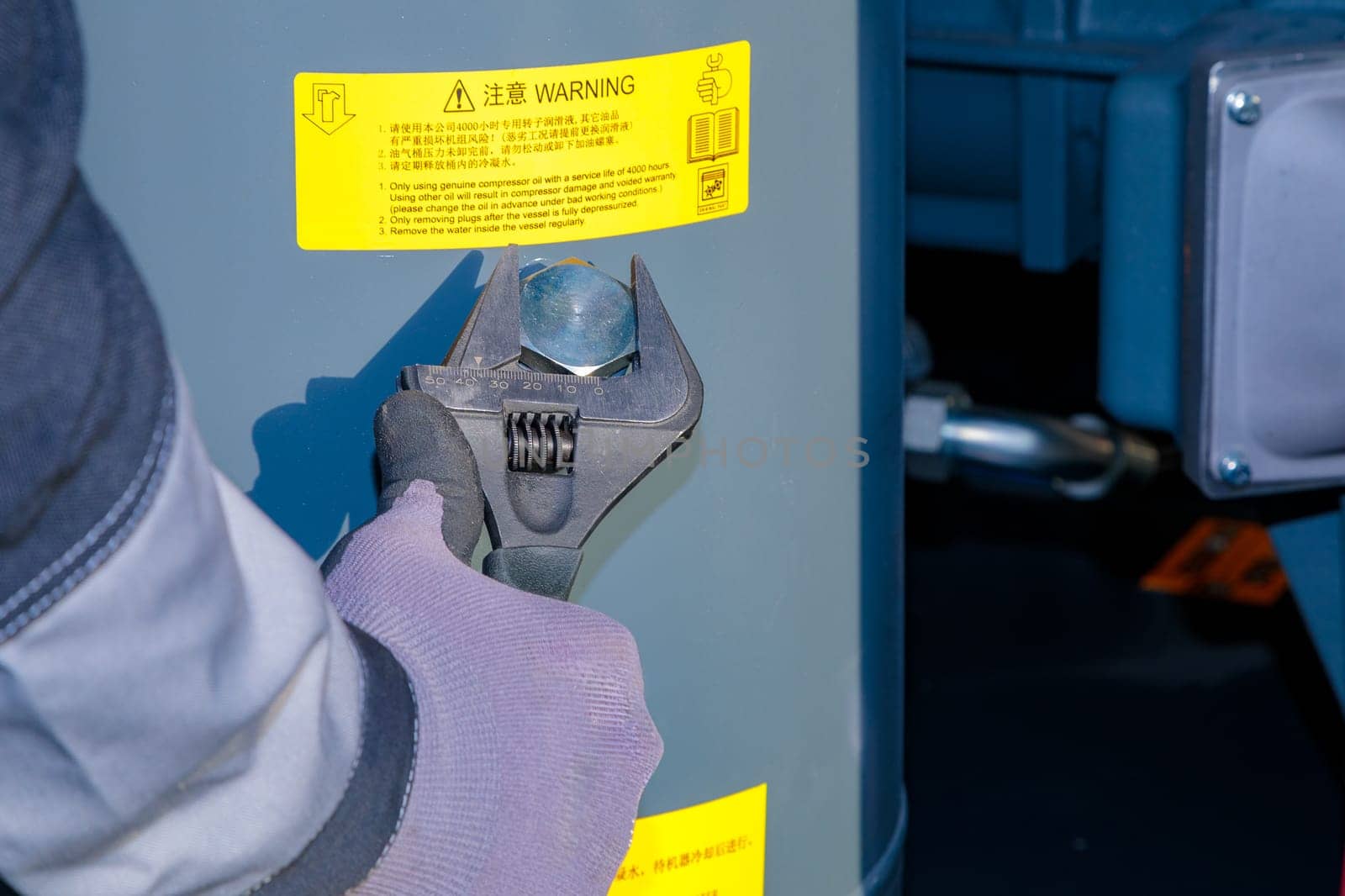 Technician is filling oil into industrial compressor using an adjustable wrench.