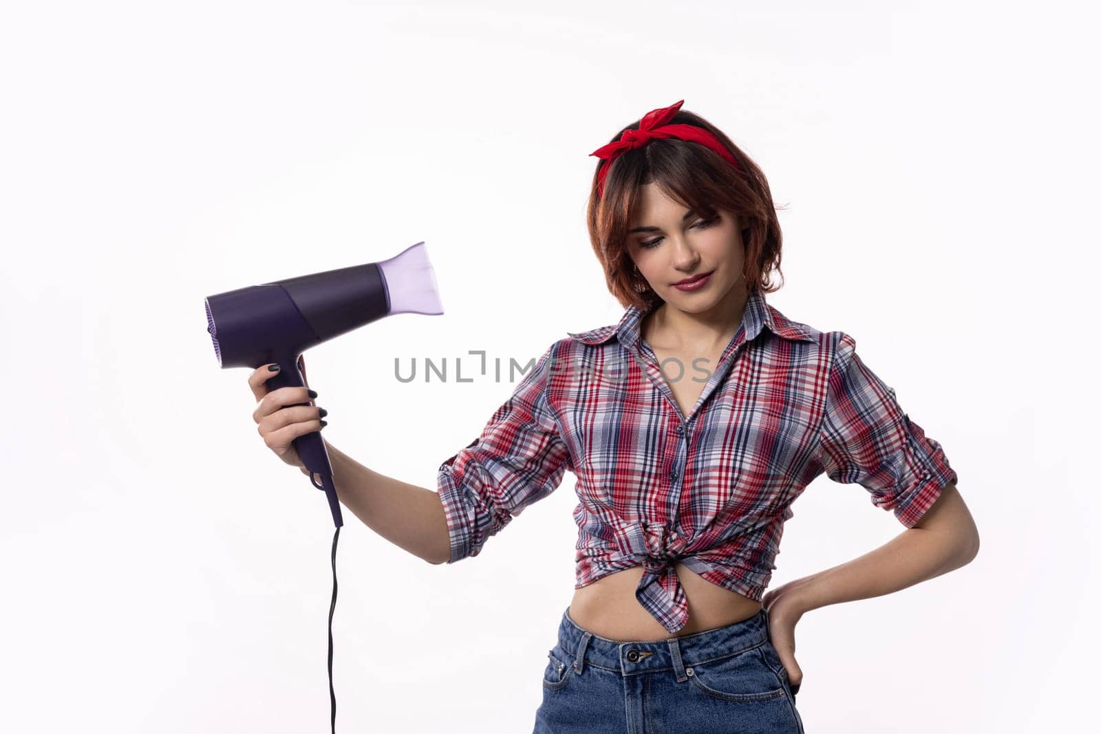 Trendy young woman confidently holding a hair dryer, showcasing a modern hairstyle and stylish outfit.
