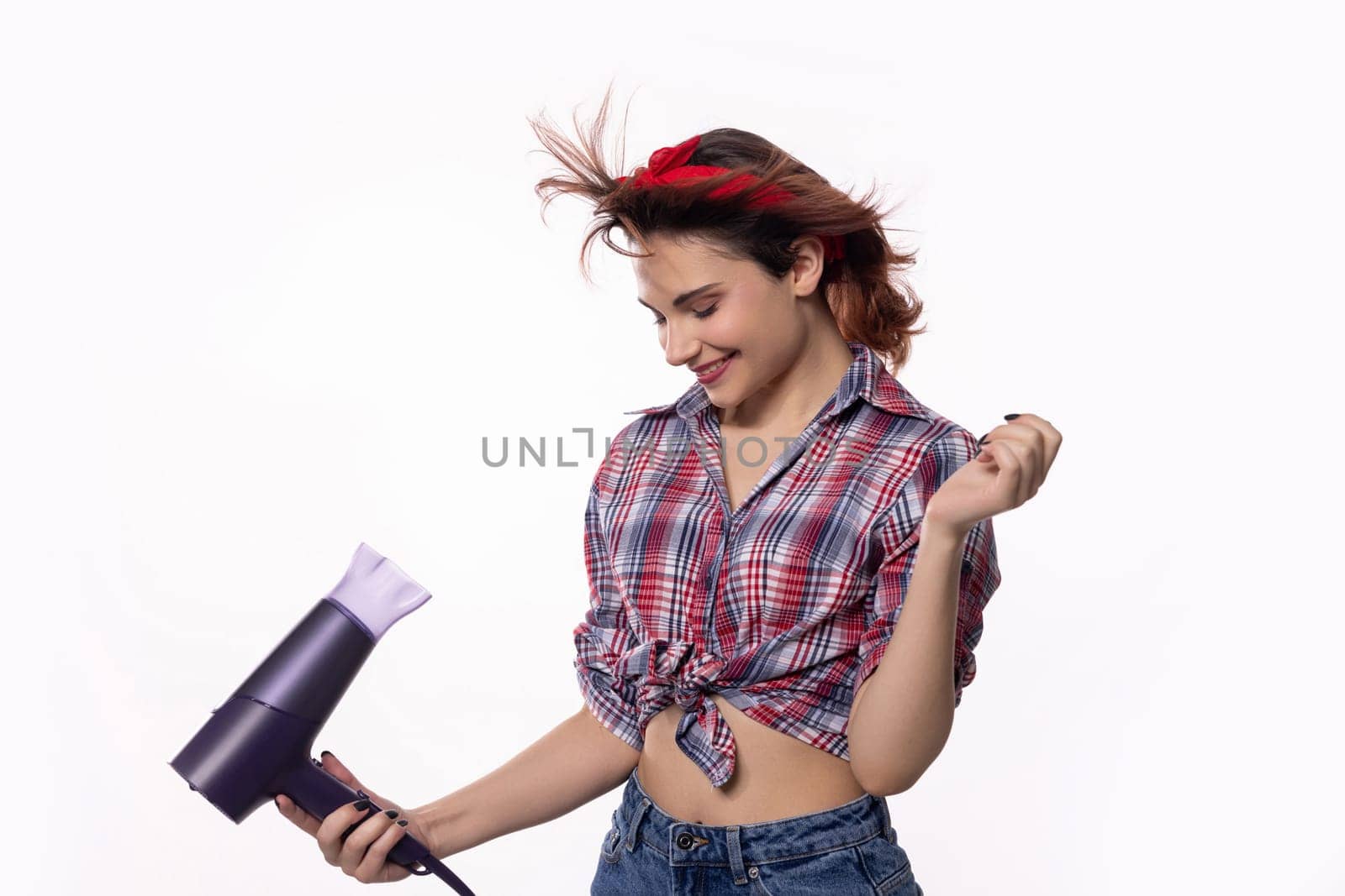A vibrant young woman is playfully using a hair dryer, showcasing her fun attitude and stylish, chic look