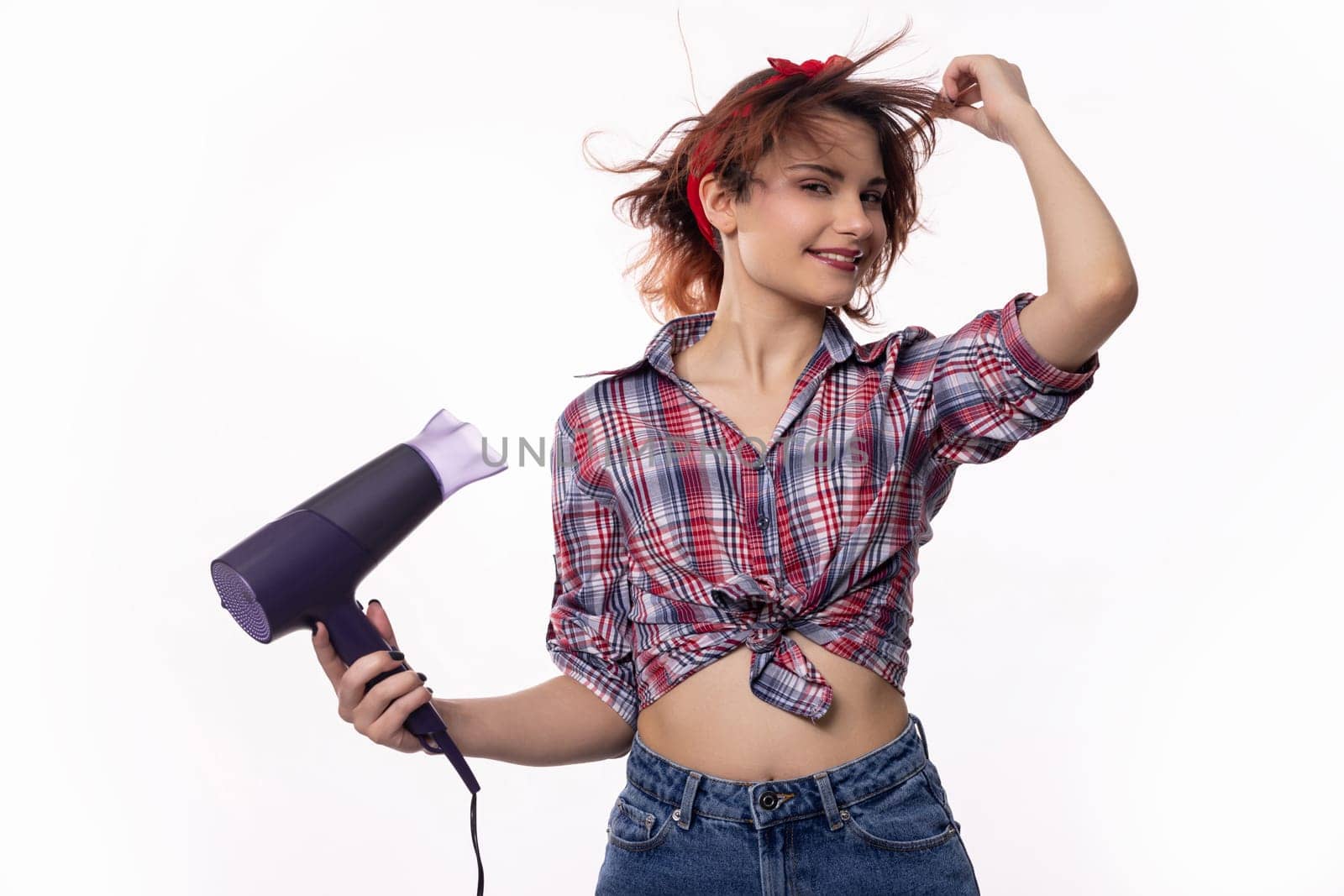 A playful young woman joyfully uses a hair dryer, delighting in her hairstyle with vibrant energy and enthusiasm