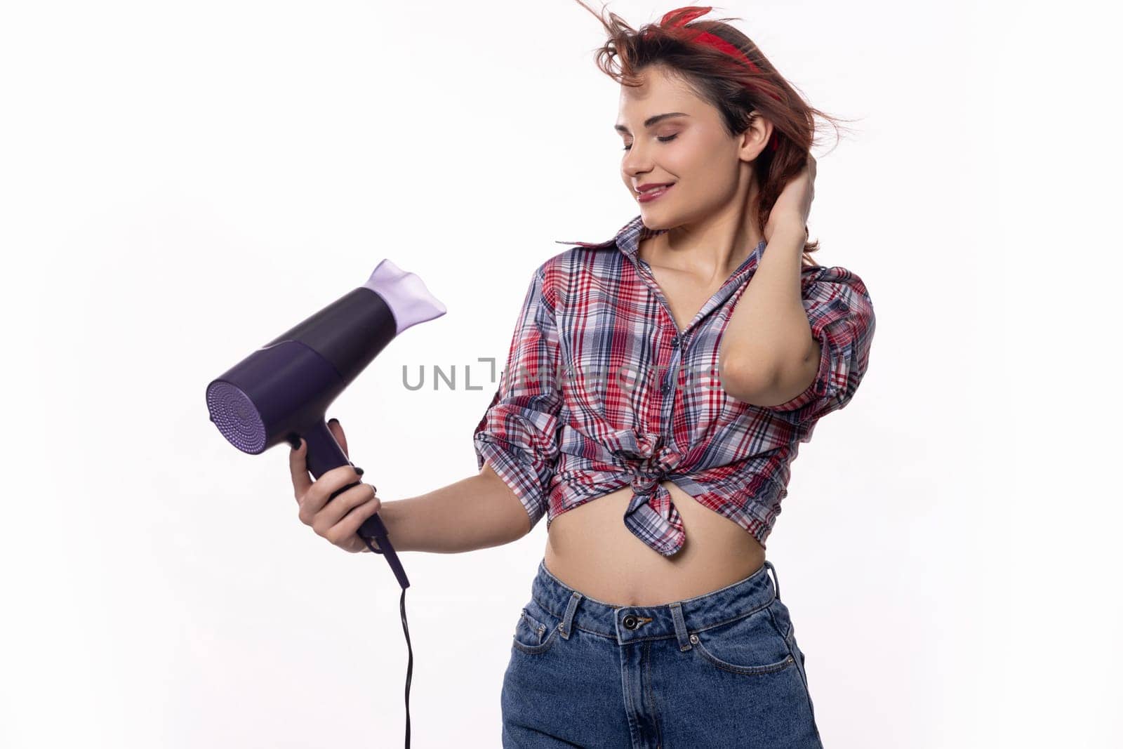 A stylish young woman is happily using a blow dryer to expertly style her beautiful hair, showcasing a trendy look