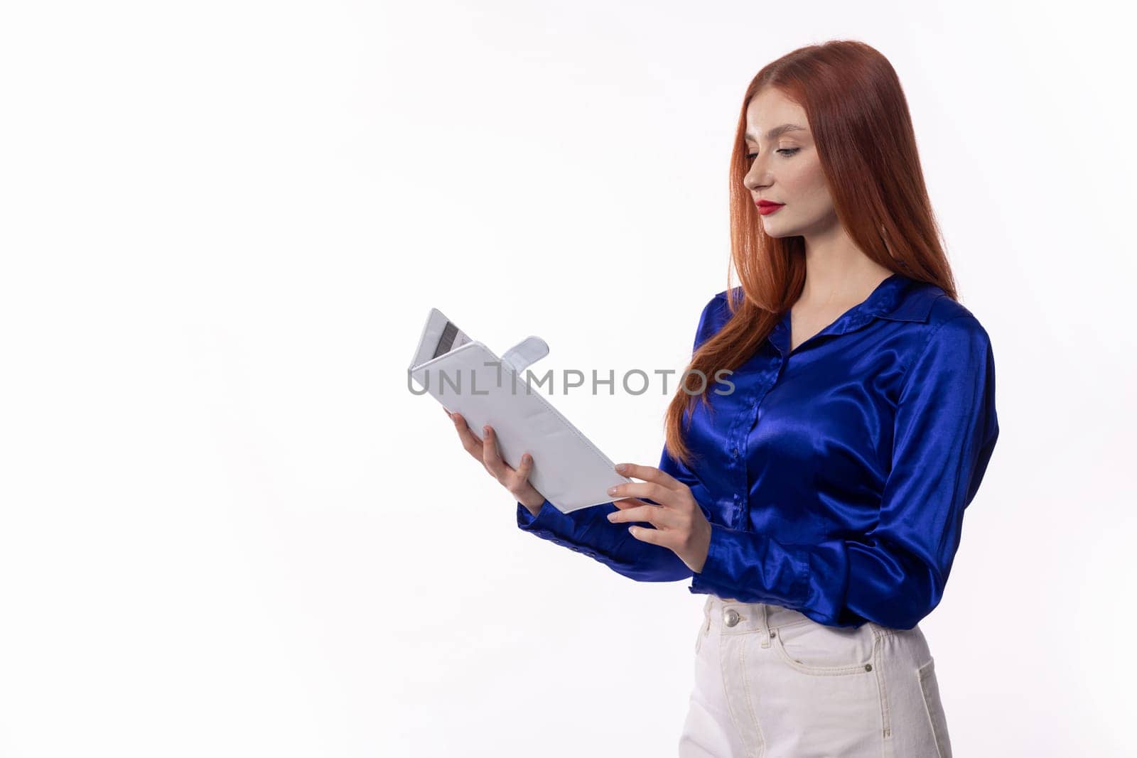 A young woman wearing a stylish blue satin shirt is deeply engrossed in reviewing a document with confidence and focus