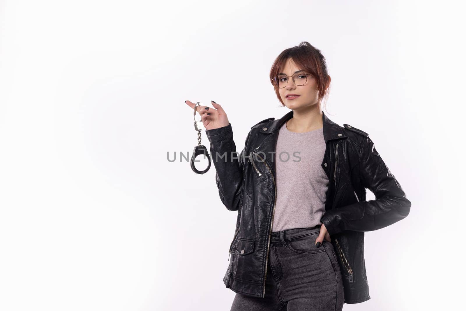 A stylish young woman with confidence holds a pair of handcuffs, showcasing her bold and playful attitude in life