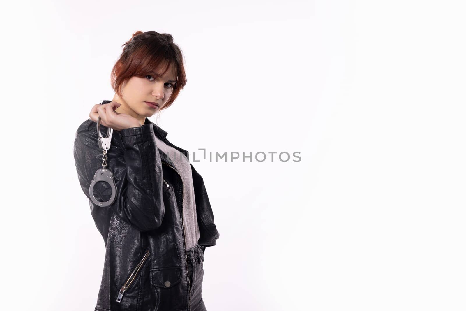 A selfassured young woman confidently holds stylish handcuffs, showcasing empowerment and flair in her chic outfit